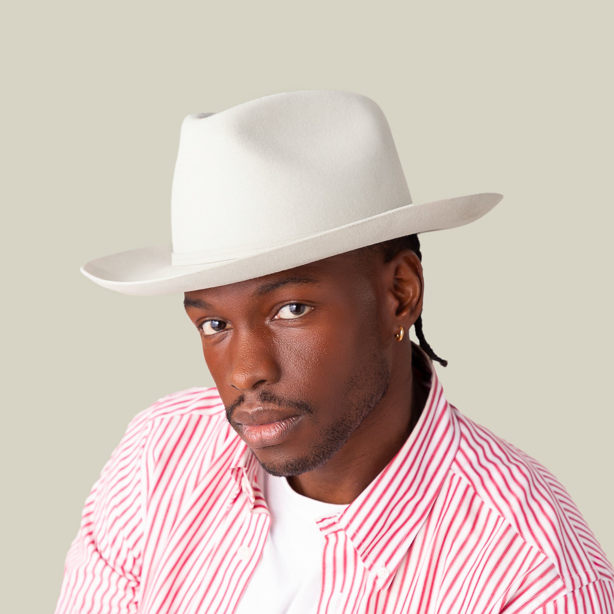 A man wearing the Goorin Bros. Night Hawk, an all-season fedora with a wide snap brim and teardrop crown, pairs it with a red and white striped shirt and white tee, posing against a plain beige background.