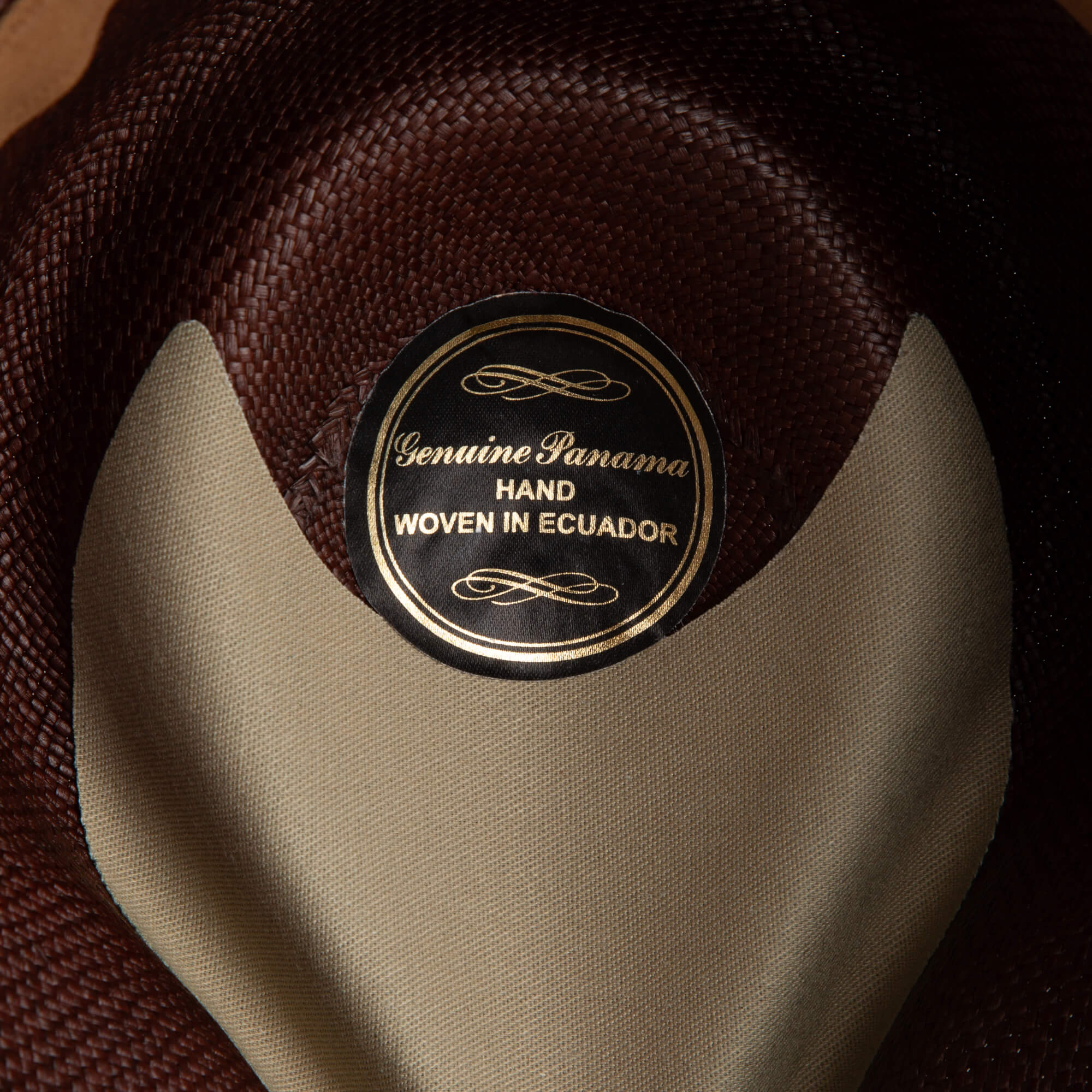 Close-up of the John Sr. fedora’s interior label by Goorin Bros., featuring decorative gold text on black reading Genuine Panama Hand Woven in Ecuador. This hat provides 50 UPF sun protection for stylish, safe outdoor wear.