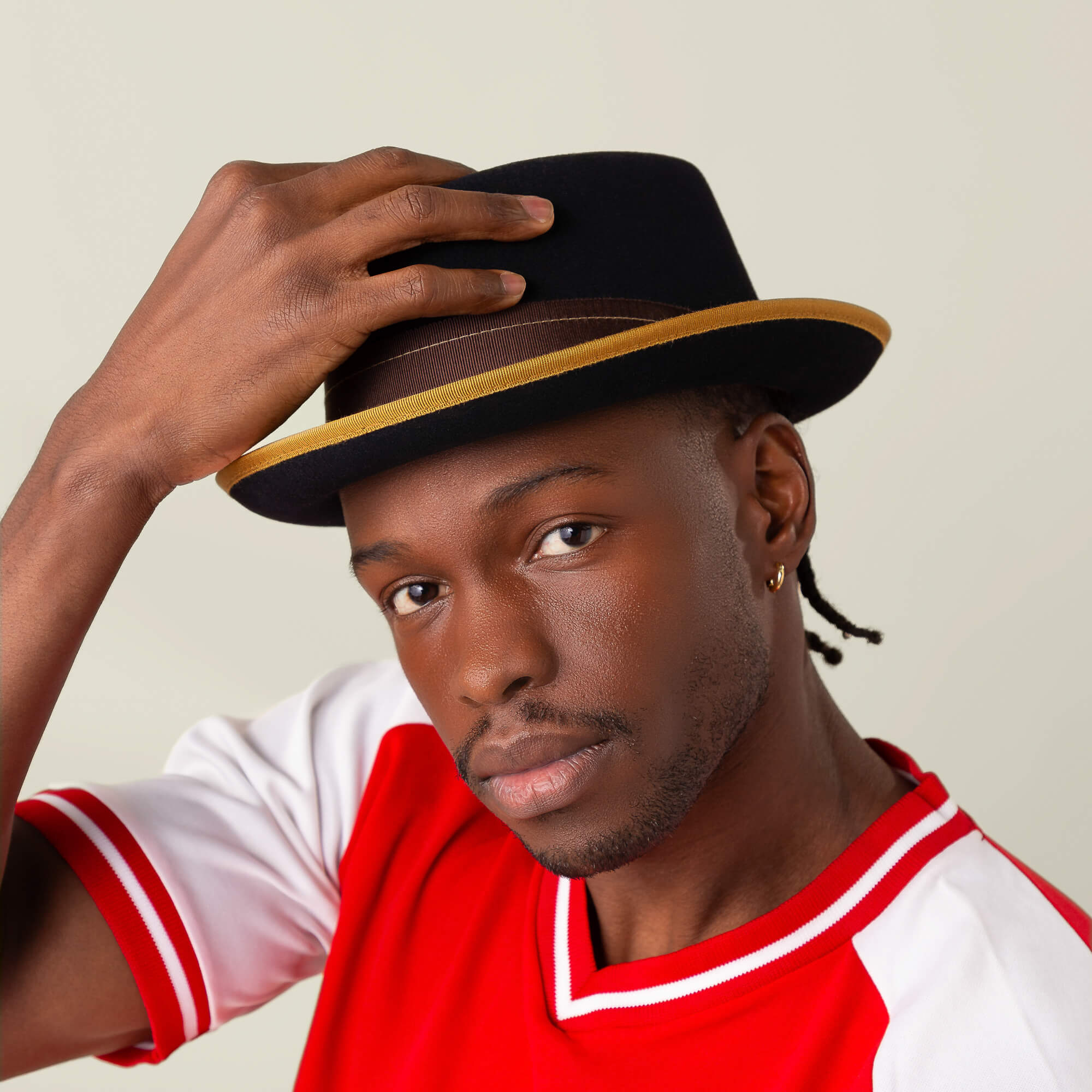 A person wears the Goorin Bros. Slick Carter black wool short brim hat with a gold band, touching the brim and looking at the camera to capture effortless style.