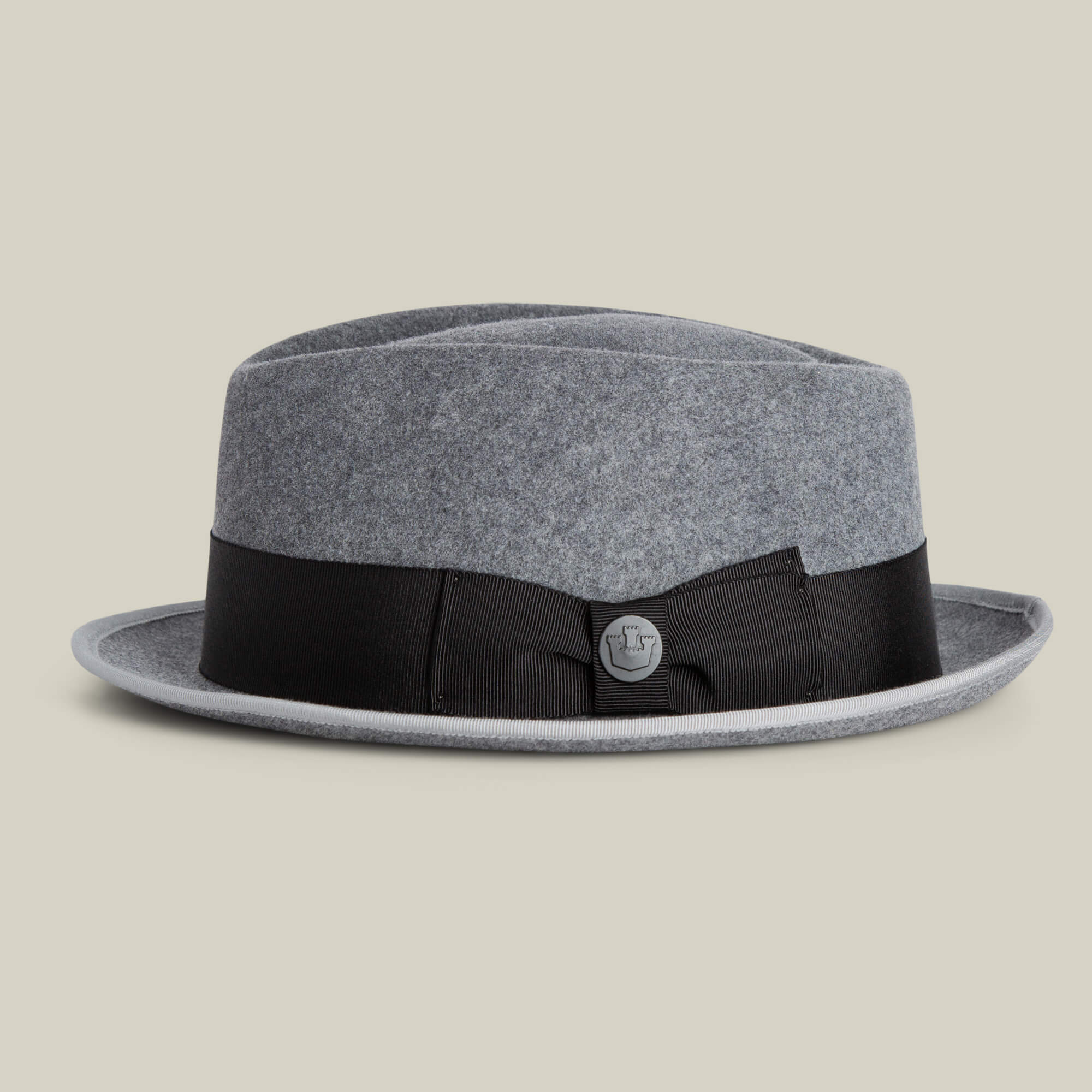 The Slick Carter by Goorin Bros. is a gray felt pork pie hat with a black ribbon band and bow, detailed with a small round emblem. Its wool short brim brings effortless style, shown here against a plain light background.
