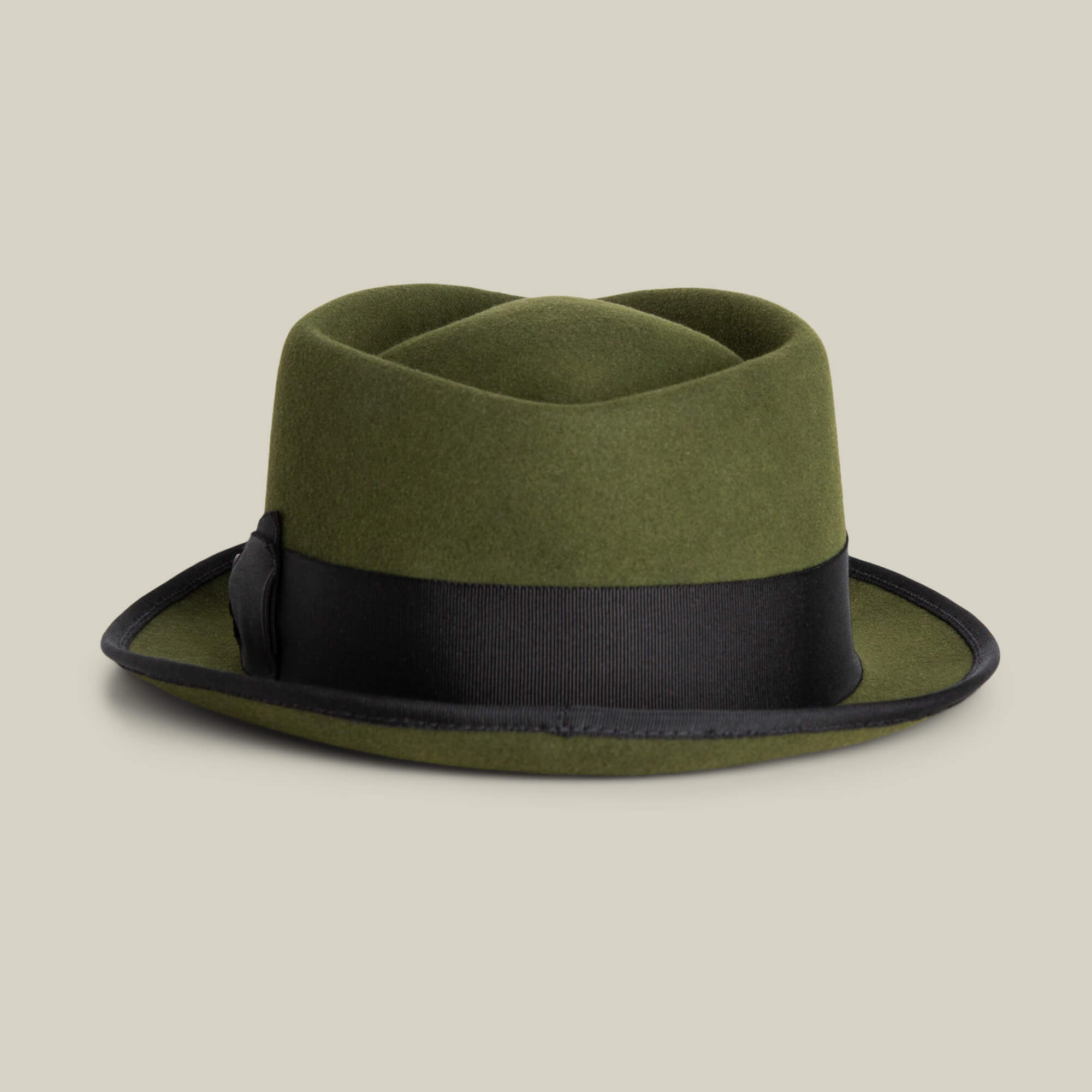 The Goorin Bros. Slick Carter is an olive green wool pork pie hat with a short, upturned brim and black ribbon band, shown on a beige background. This stylish piece adds charm to any outfit.