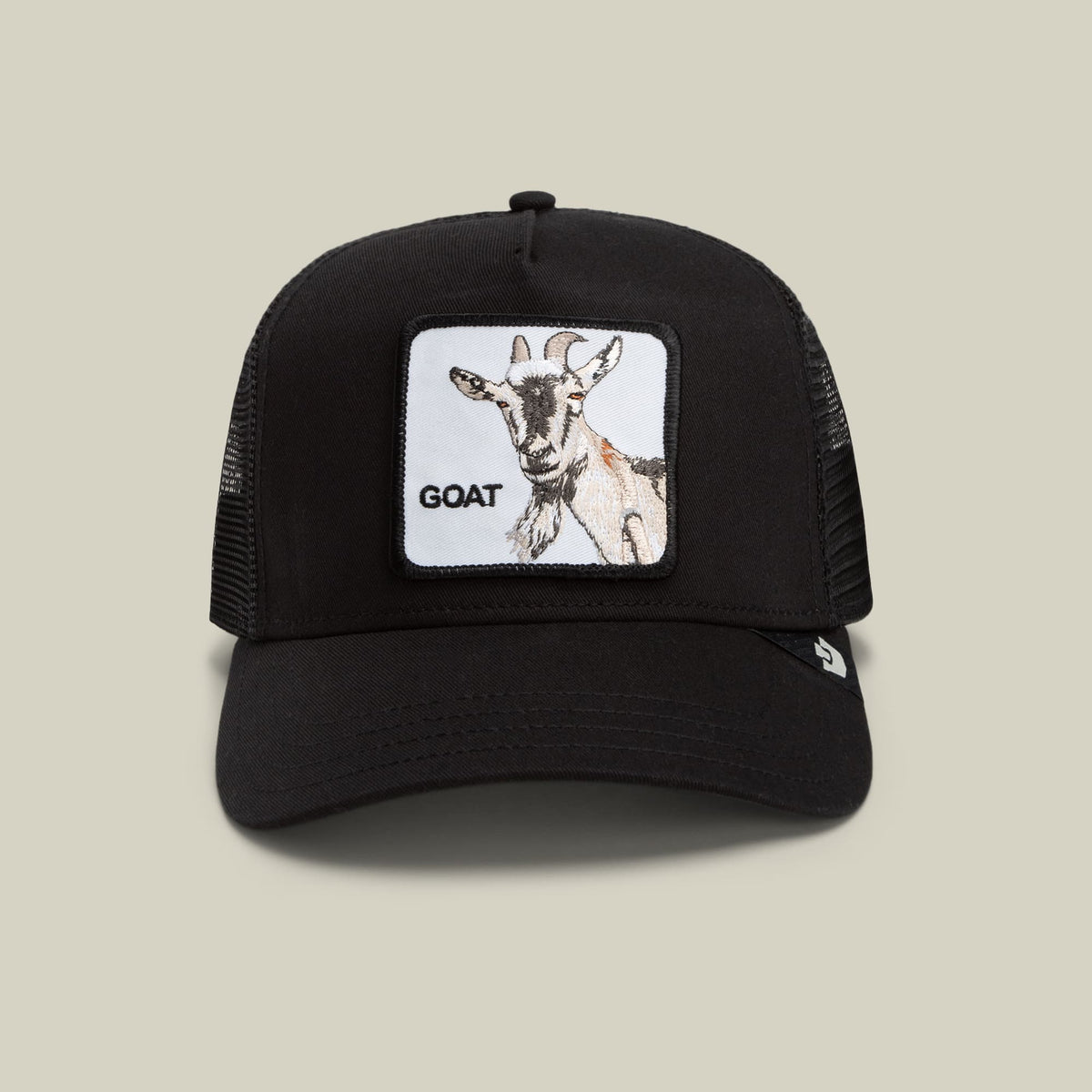 The Goorin Bros. Goat Beard is a black trucker hat with a mesh back panel and a white patch featuring an illustrated goat and text reading "GOAT" on the front, shown against a neutral beige background.