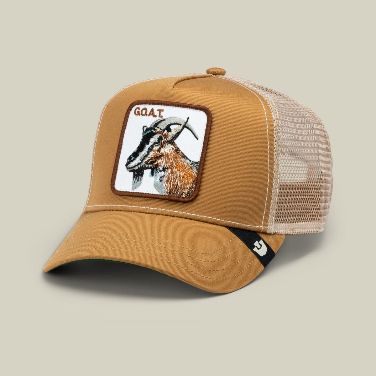 The GOAT by Goorin Bros. is a tan and cream trucker hat with a mesh back panel, featuring an embroidered goat patch on the front and an adjustable snapback closure.