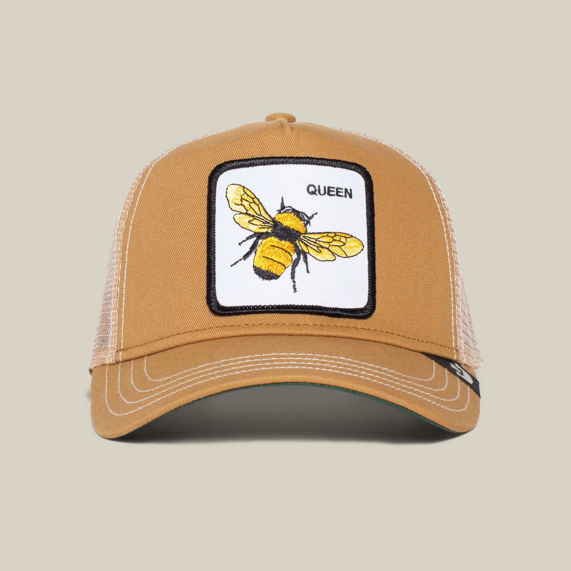 The Farm’s "The Queen Bee" tan trucker hat features a mesh back and a front patch with a yellow and black bee crowned by the word QUEEN—ideal for anyone ready to slay every day.