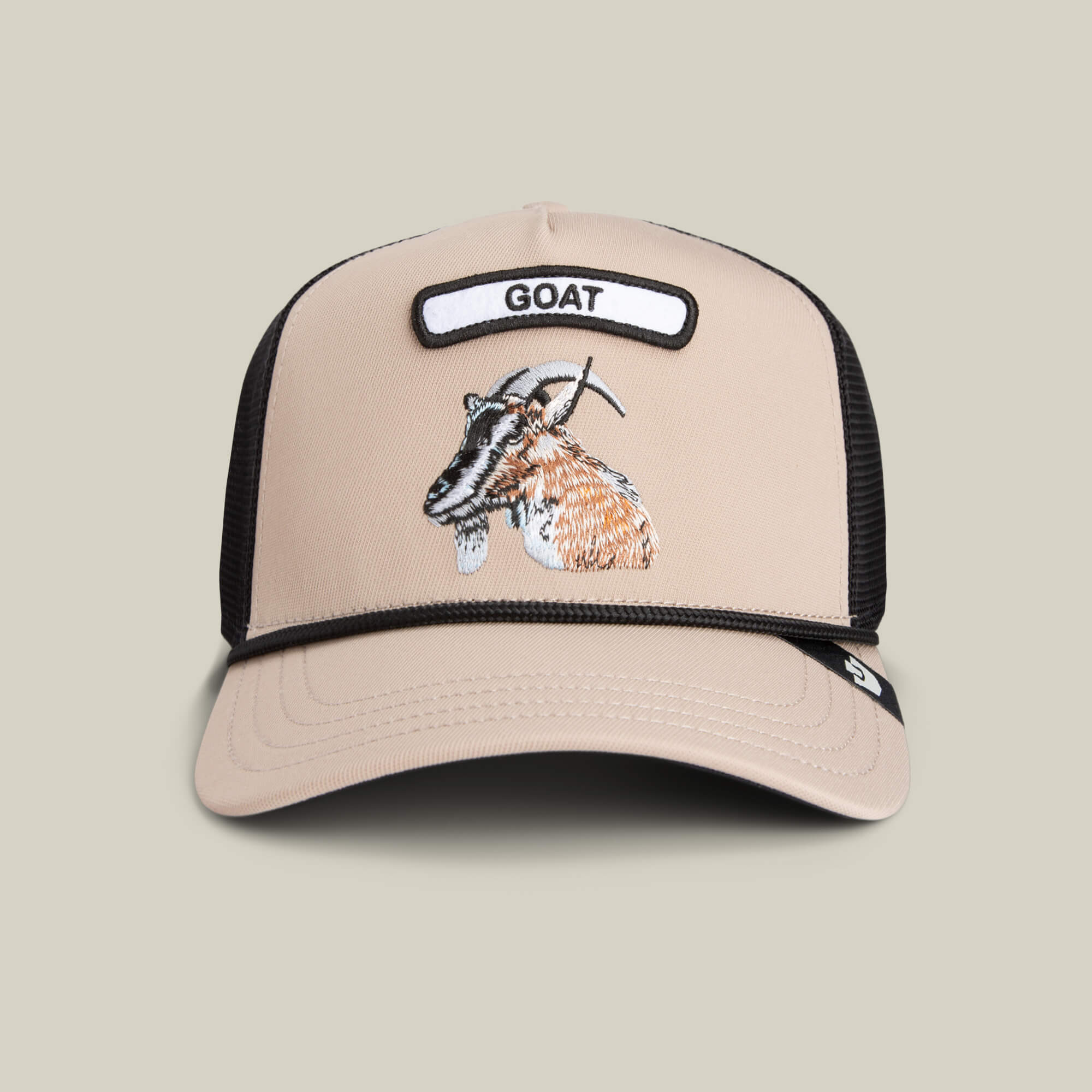 The Farm’s GB2 Goat Trucker Hat in beige and black features a mesh back, an embroidered goat, and a front patch labeled GOAT—a bold badge of honor for champions.