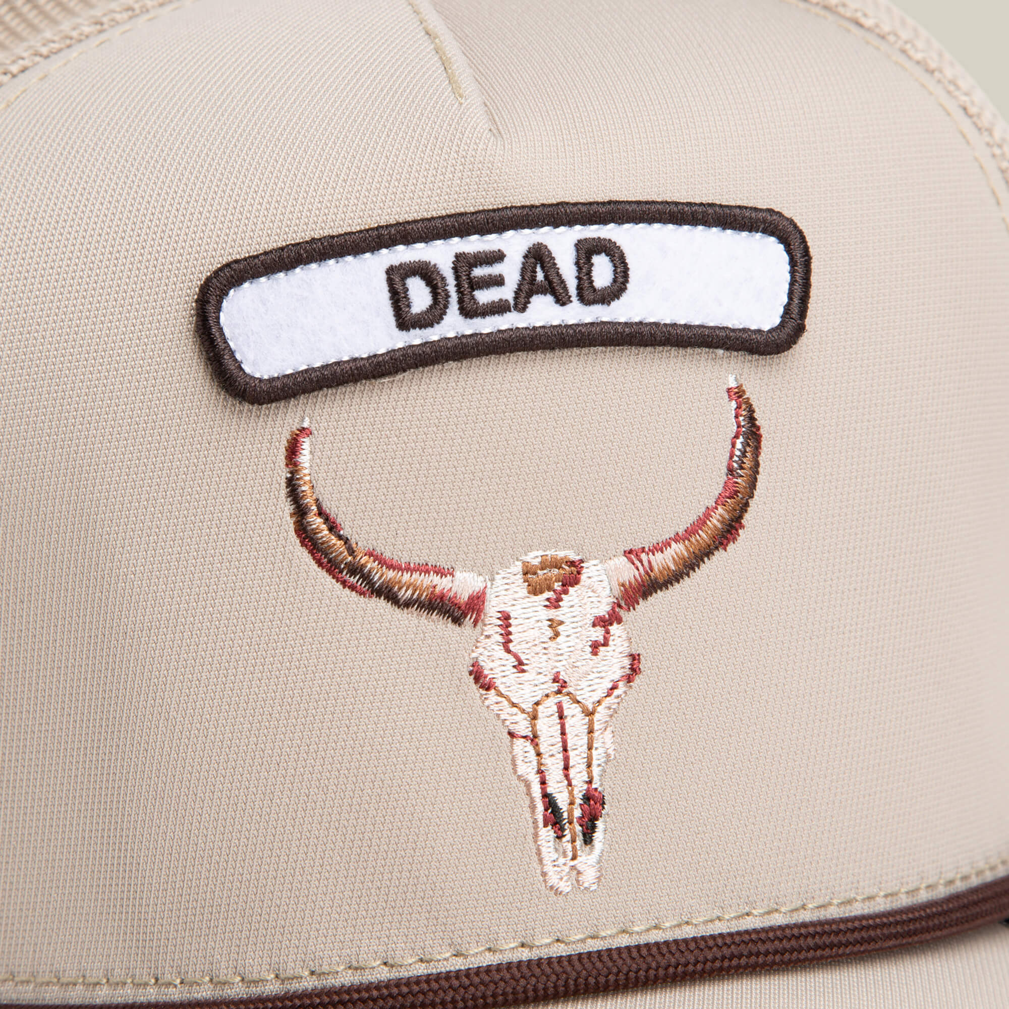 The GB2 Skull by Goorin Bros. is a beige trucker hat with desert tones, featuring an embroidered cattle skull patch and a bold "DEAD" patch above it.