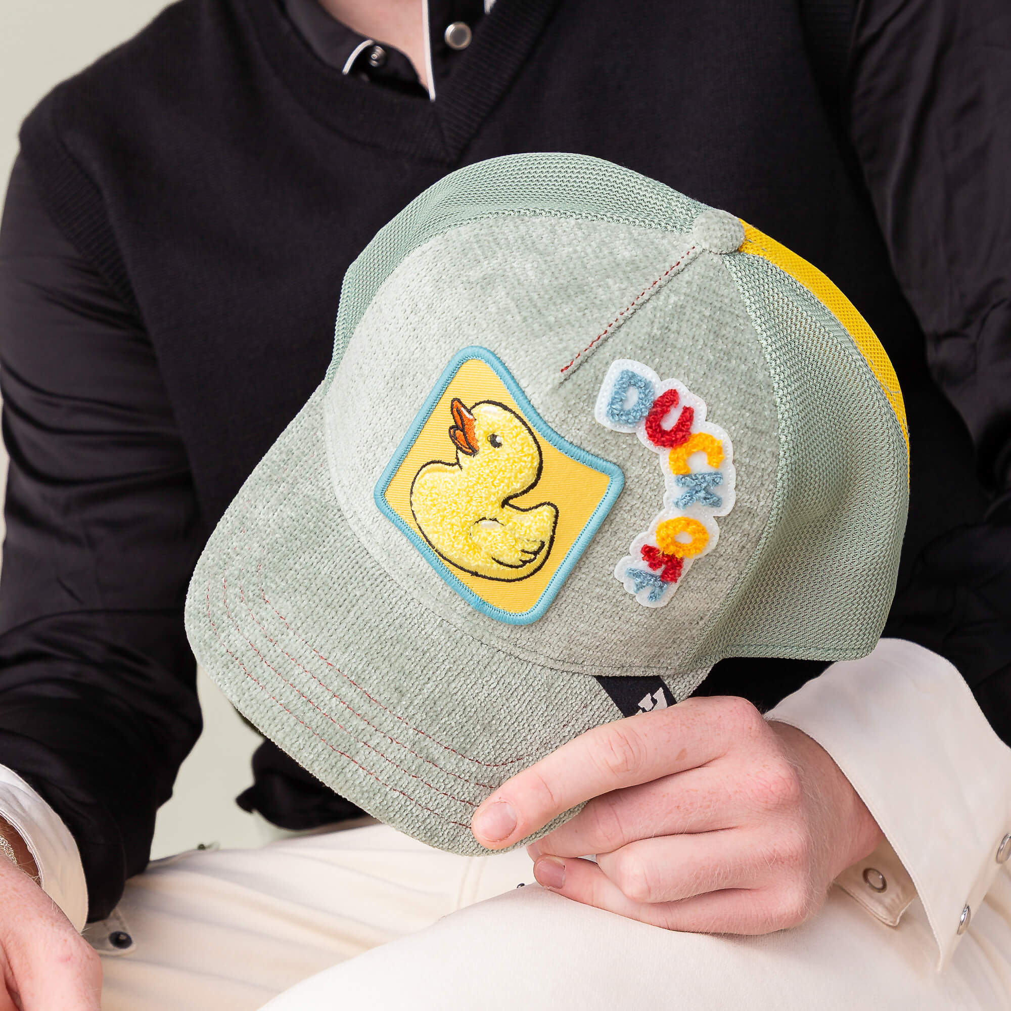 Person holding a Goorin Bros. Ducking Autocorrect hat, a light gray mesh cap featuring a yellow rubber duck patch and "DUCK" in colorful letters—a fun novelty addition to any hat collection.