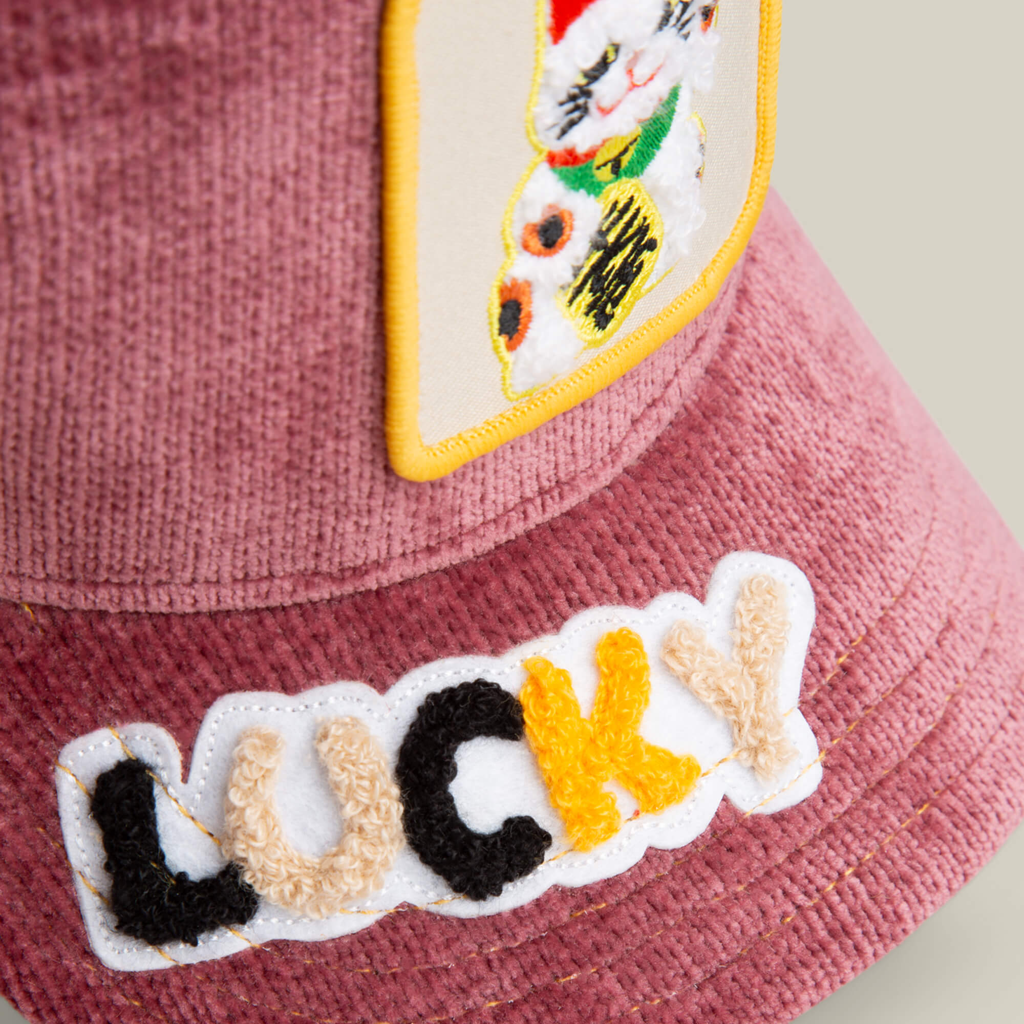 A close-up of the Goorin Bros. "Maneki-Neko" pink corduroy plush hat with an embroidered beckoning cat patch and a fuzzy "LUCKY" patch in black, cream, and yellow letters.
