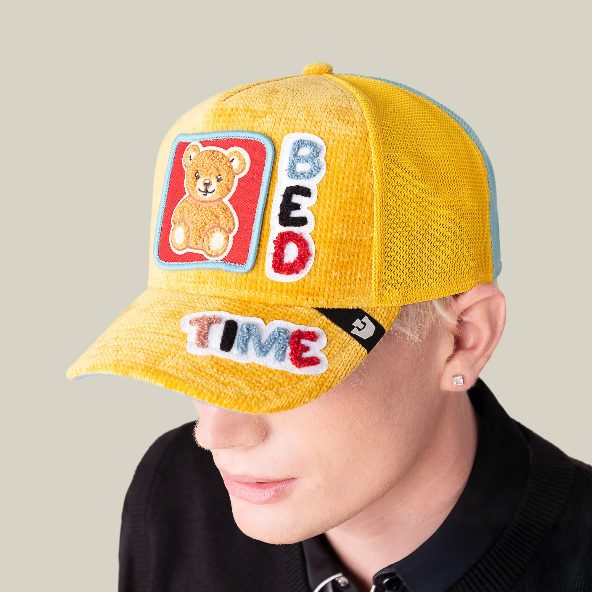 A person wears the Goorin Bros. Duvet All Det sunshine yellow hat with a teddy bear patch and "BED TIME" in colorful letters, paired with a black collared shirt against a plain background.