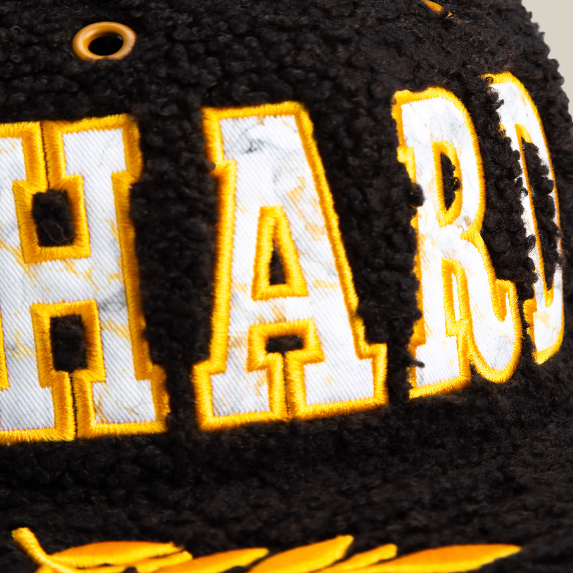 Close-up of the Goorin Bros. Marble Madness cap, featuring black sherpa texture with large yellow and white embroidered "HARD" on the front and subtle gold accents.