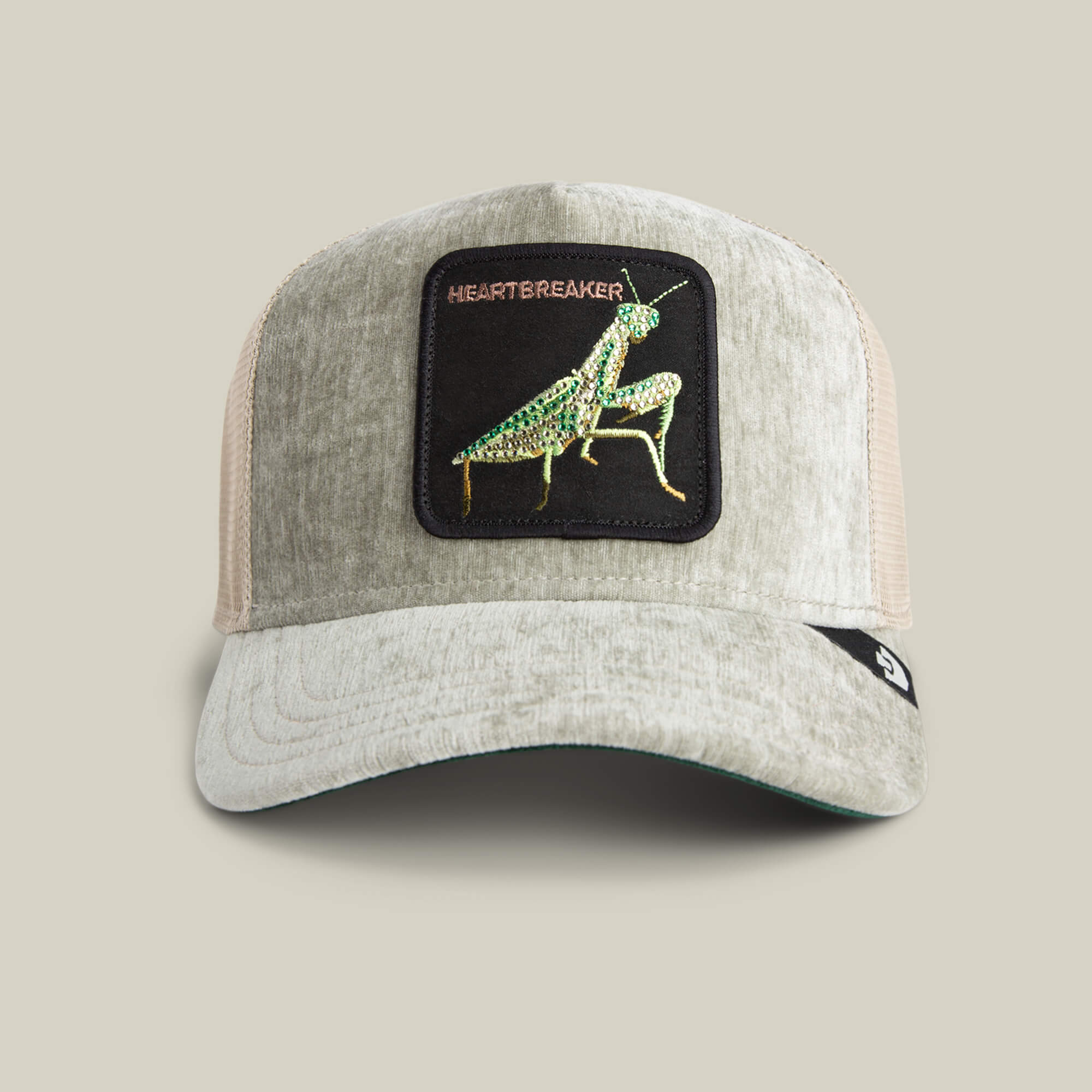 The Goorin Bros. Iced Mantis SHADE trucker hat features a light gray and beige design, a champagne mesh back, and a patch with a green Praying Mantis plus HEARTBREAKER embroidered above it.