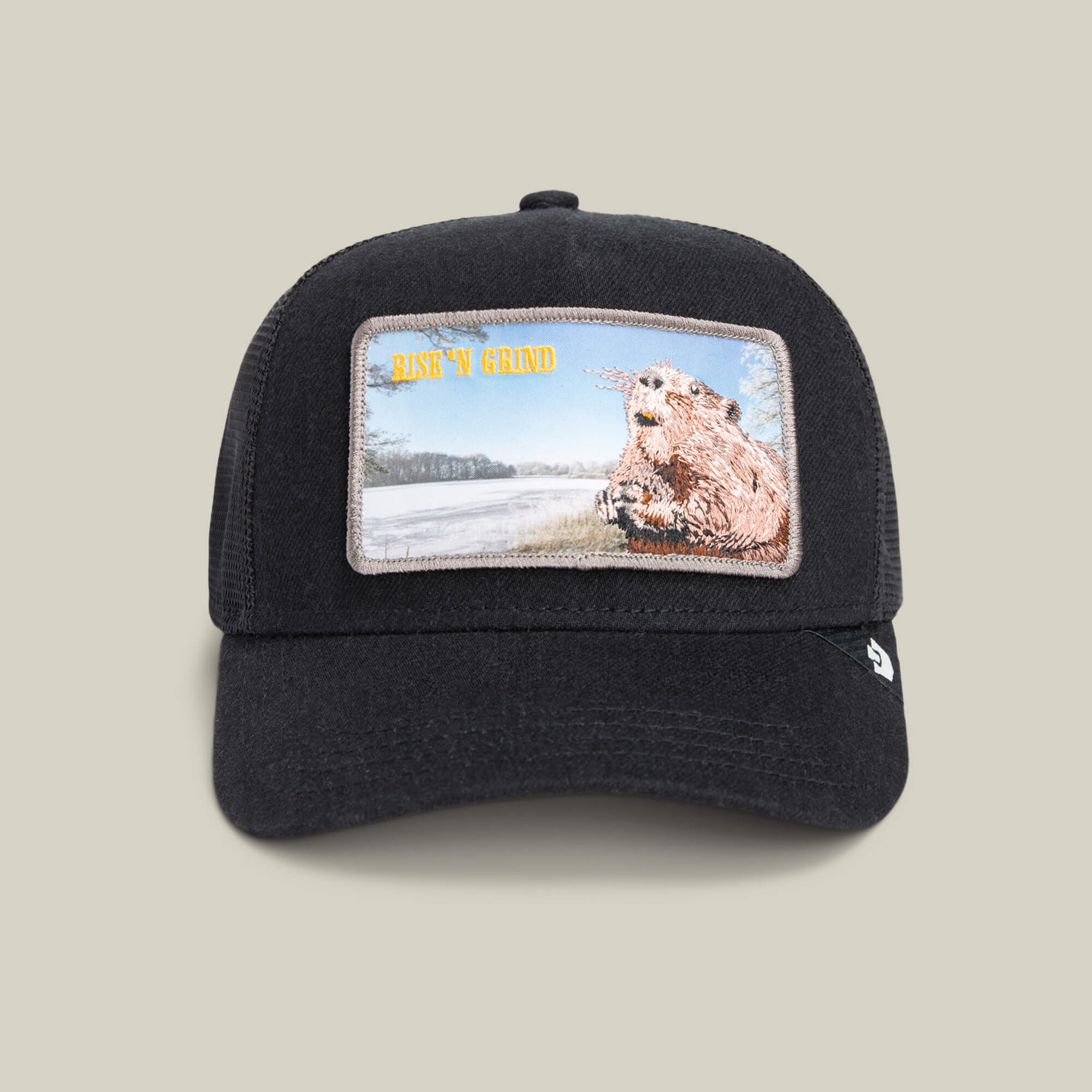The Morning Wood by Goorin Bros. is a dark denim mesh trucker hat featuring a capybara patch, RISE N GRIND text, and field-and-sky backdrop for upbeat energy.