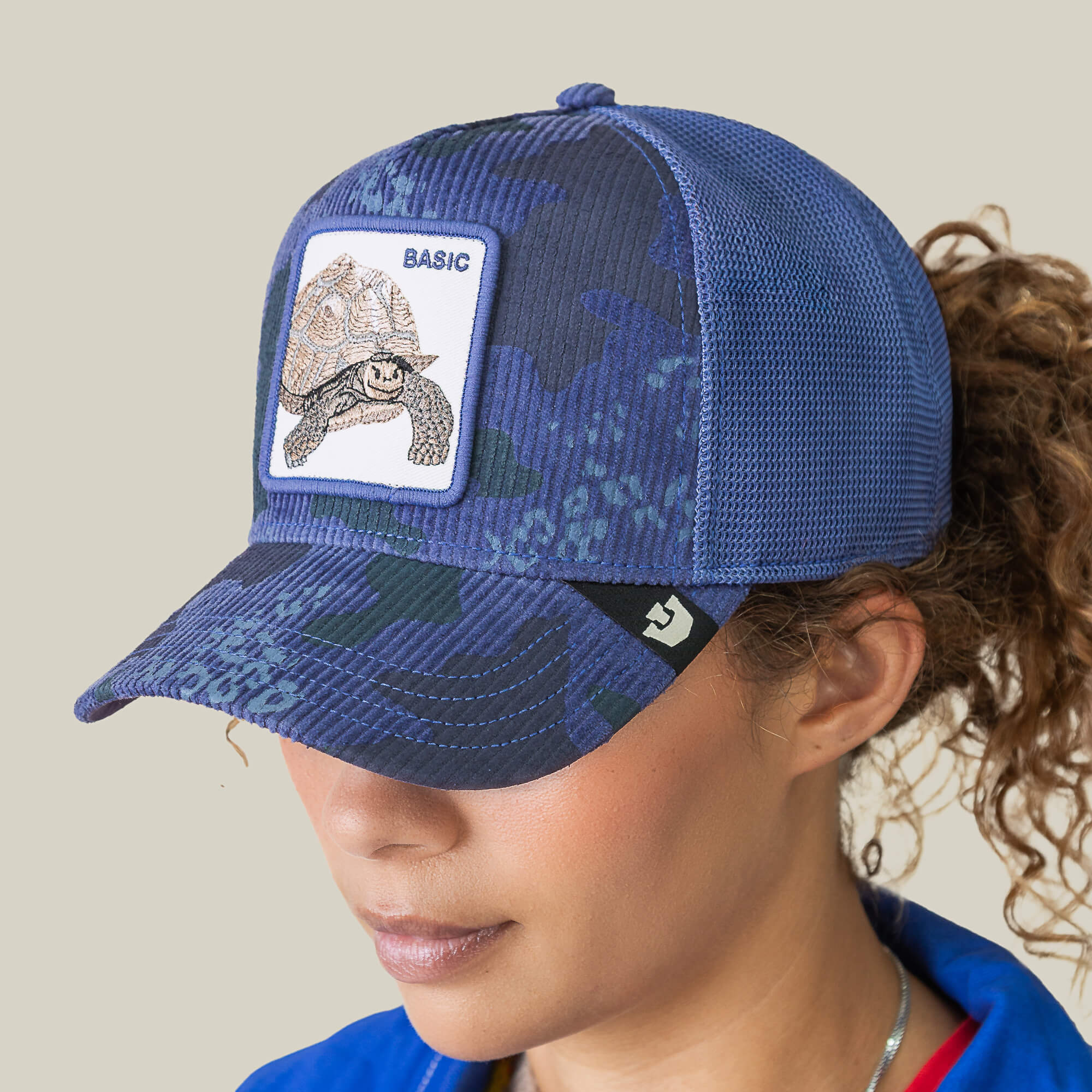 A person wears the Goorin Bros. Turtle Camo cap, a blue camo corduroy hat with a mesh back and a patch featuring a tortoise and the word "BASIC.