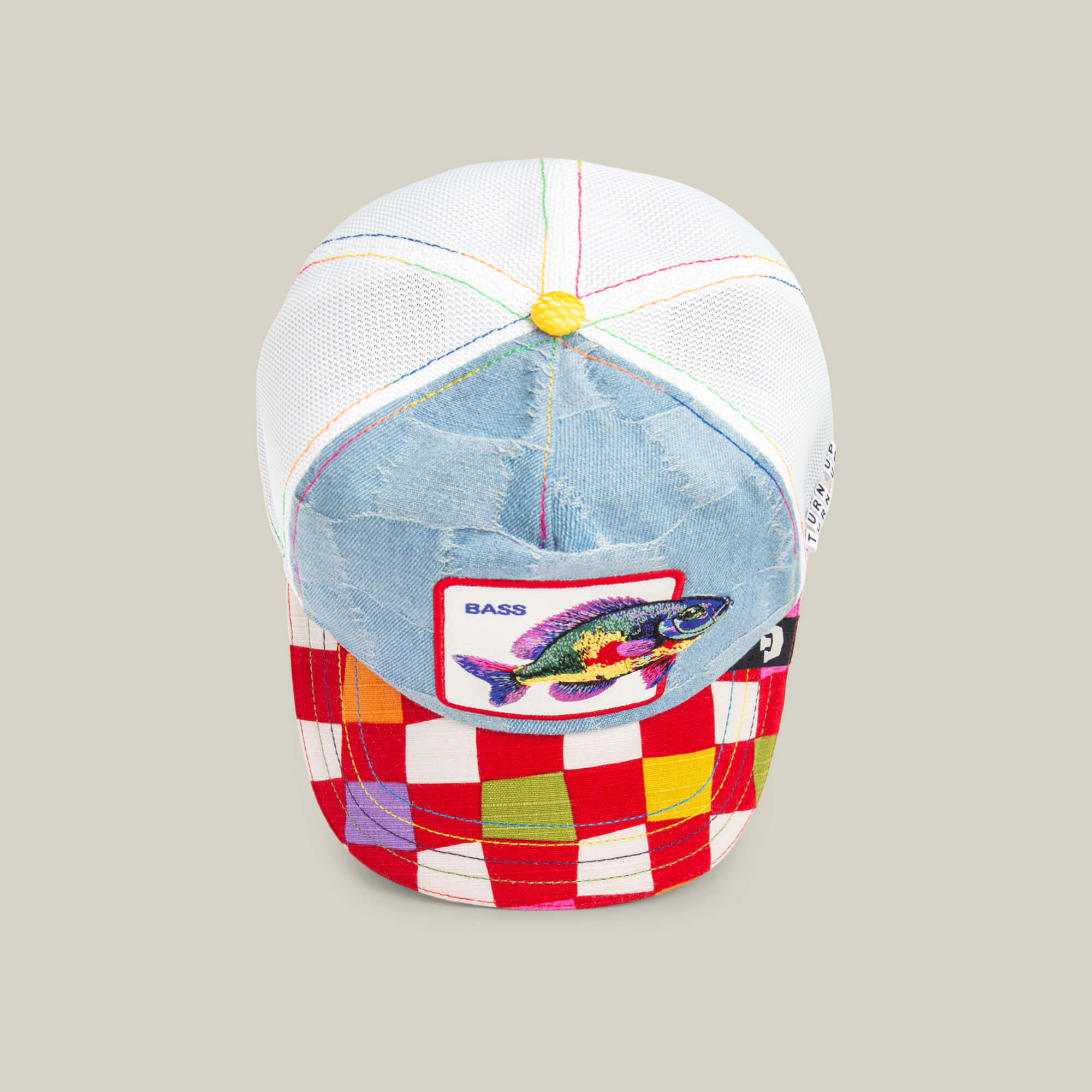 The Goorin Bros. Drum and Bass trucker hat features a denim front, mesh back, multicolored stitching, “BASS” fish patch, and a red-white checkered brim with yellow accents—perfect for bass music lovers at a festival.