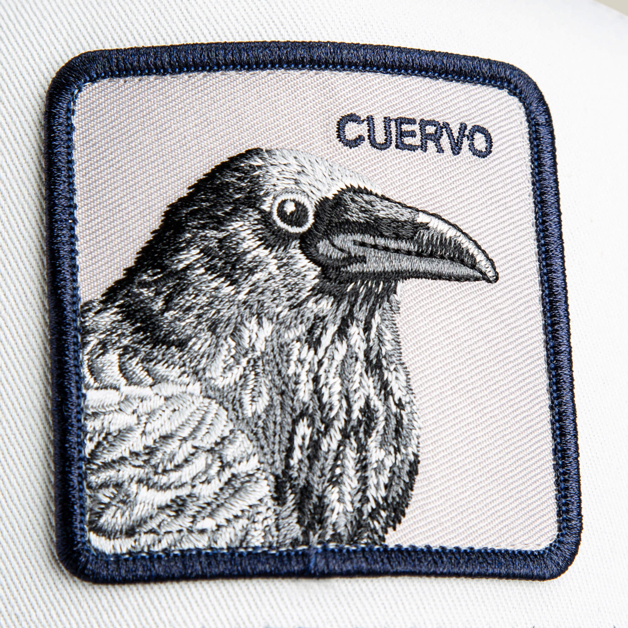 The Goorin Bros. Tricolor Raven patch features a detailed black and white raven and the word CUERVO stitched in the top right—ideal for personalizing a white crown hat or navy bill cap.