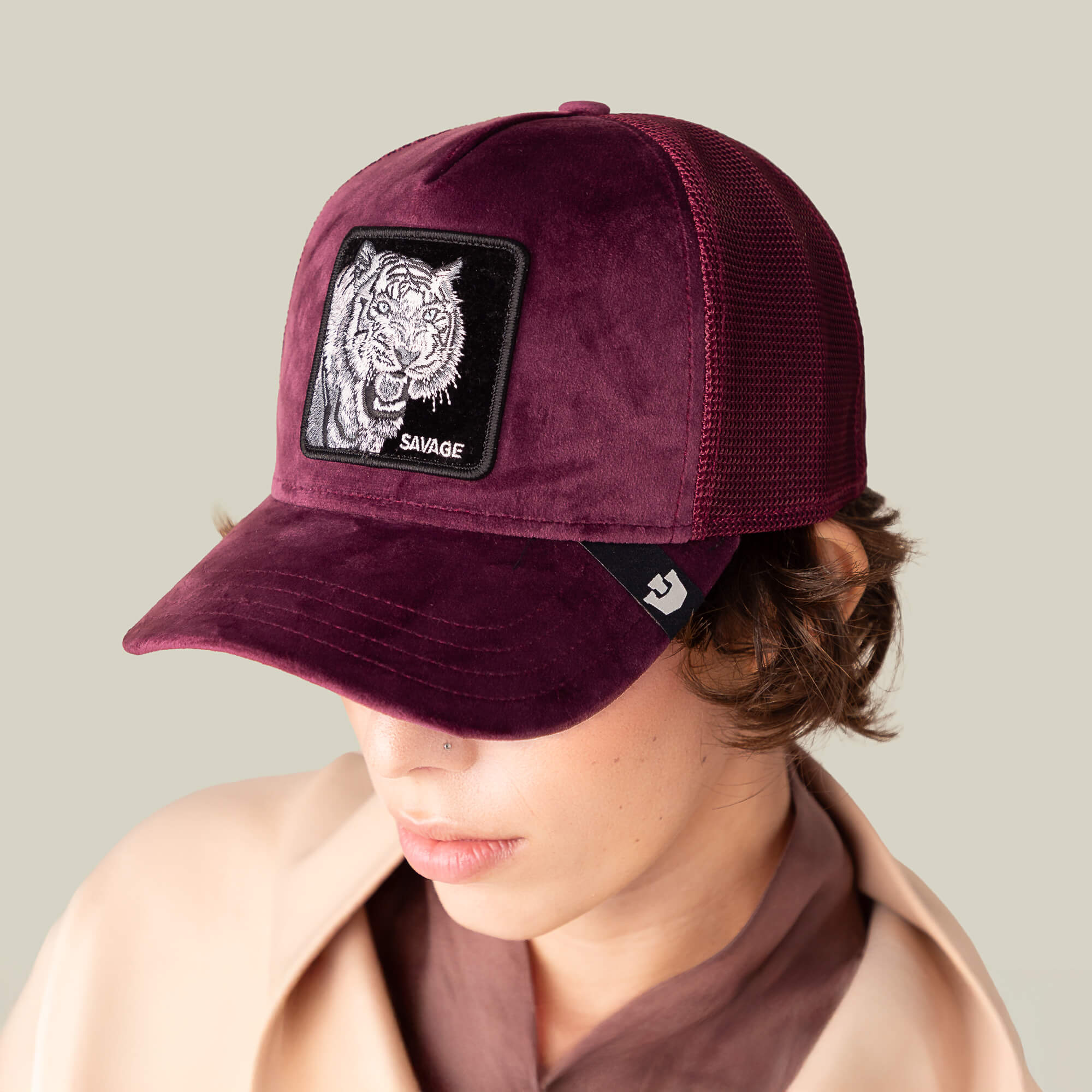 A person wears the Goorin Bros. Velour Tiger cap in deep wine mesh, featuring a SAVAGE patch, while looking down against a plain light background.