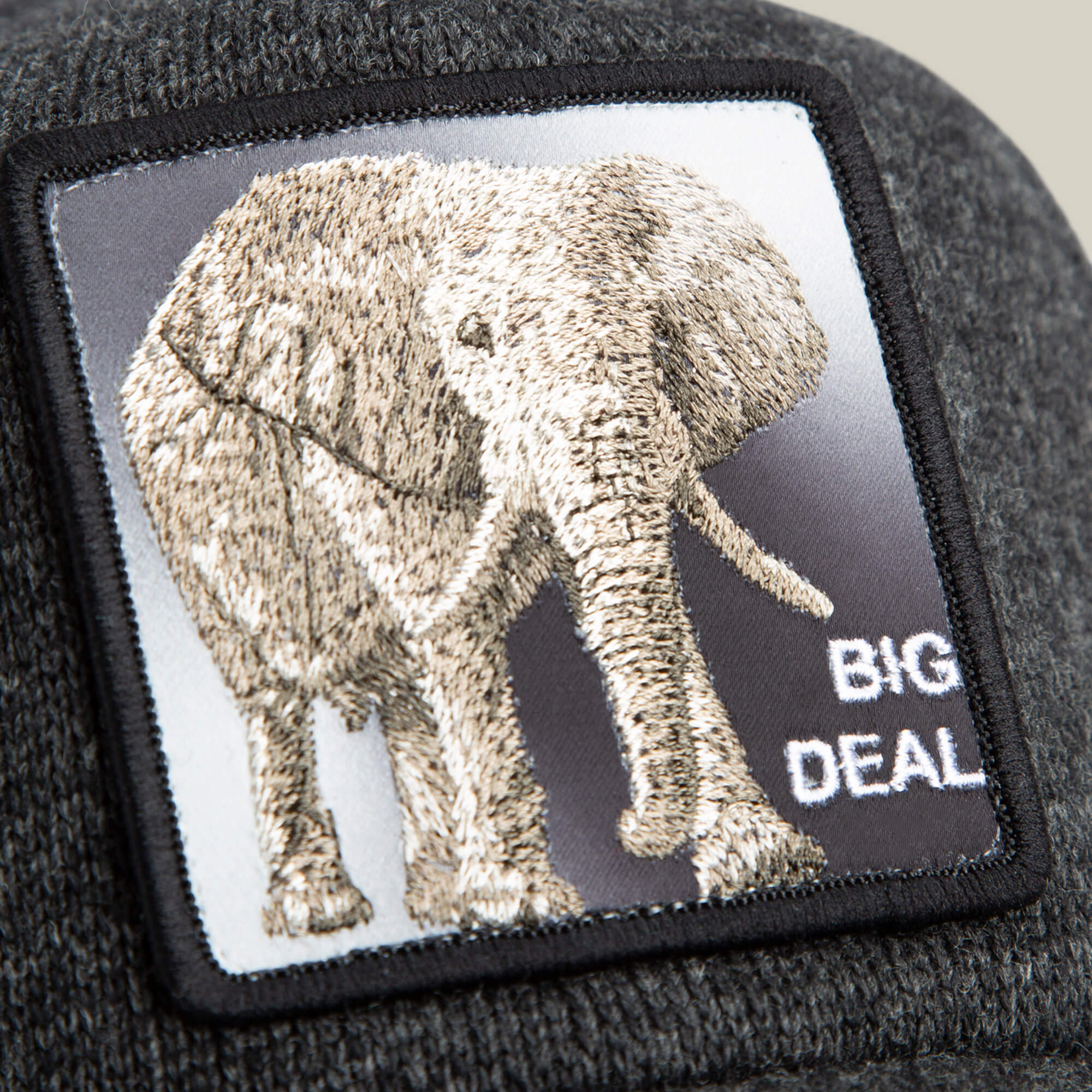 Close-up of a gray trucker beanie hat by Goorin Bros., called "Kind of," featuring an embroidered elephant, BIG DEAL text, and crafted from epic sweater material for ultimate comfort.