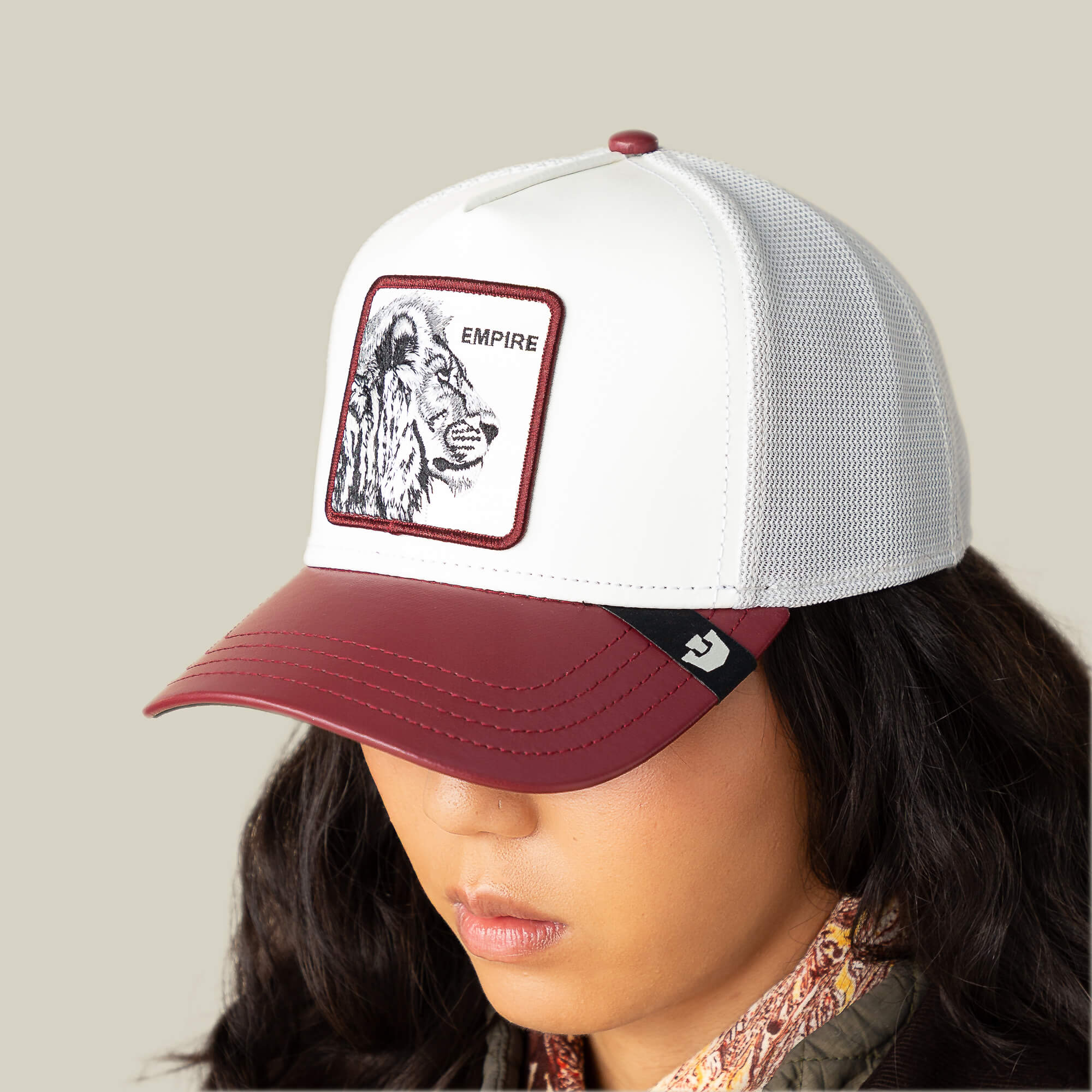 A person wears the Goorin Bros. Courtside Empire trucker hat, featuring a leather-look crown and an EMPIRE lion patch, ideal for sneaker culture fans, set against a plain beige background.