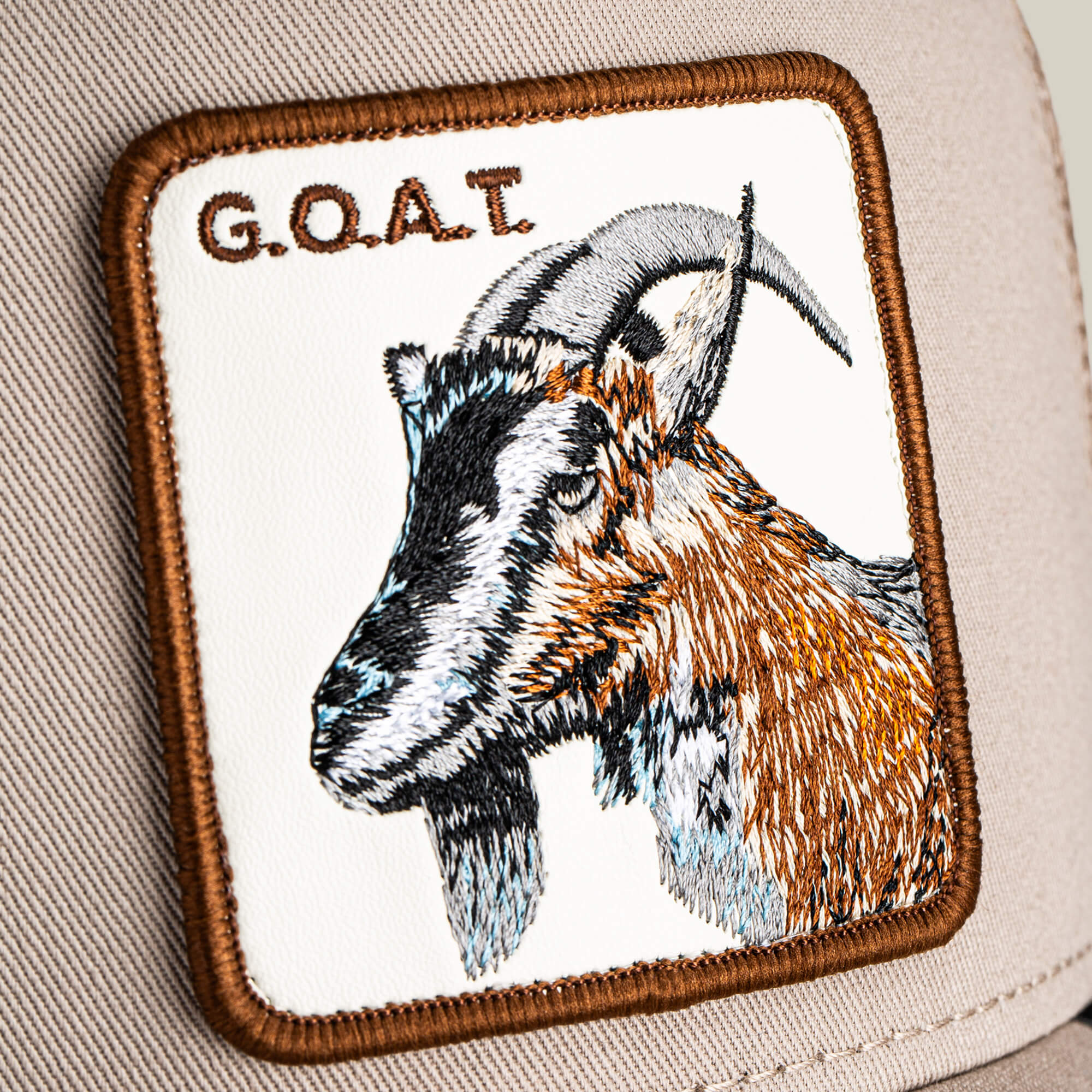 Close-up of The G.O.A.T by Goorin Bros., a neutral-tone hat with a bold embroidered patch showing a goat and the text "G.O.A.T" at the top.