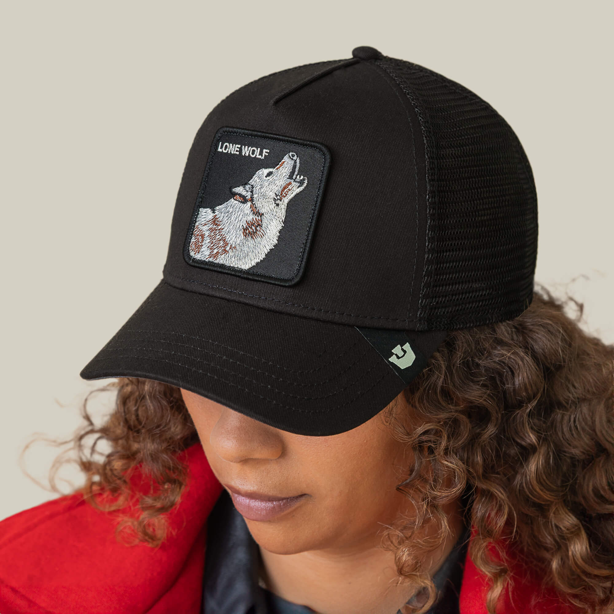 Wearing The Lone Wolf hat by Goorin Bros., a person with brown curls and a red jacket exudes outlaw energy against a plain background.