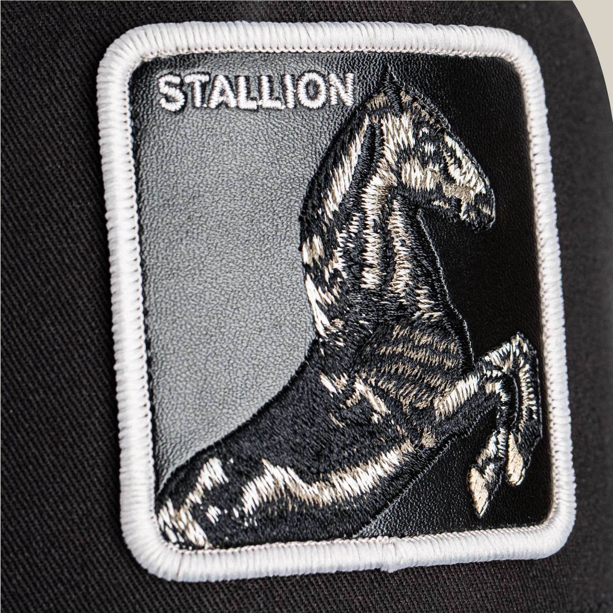 The Goorin Bros. Stallion Trucker is a black and white hat featuring an embroidered rearing horse with the word "STALLION" on a black fabric patch.