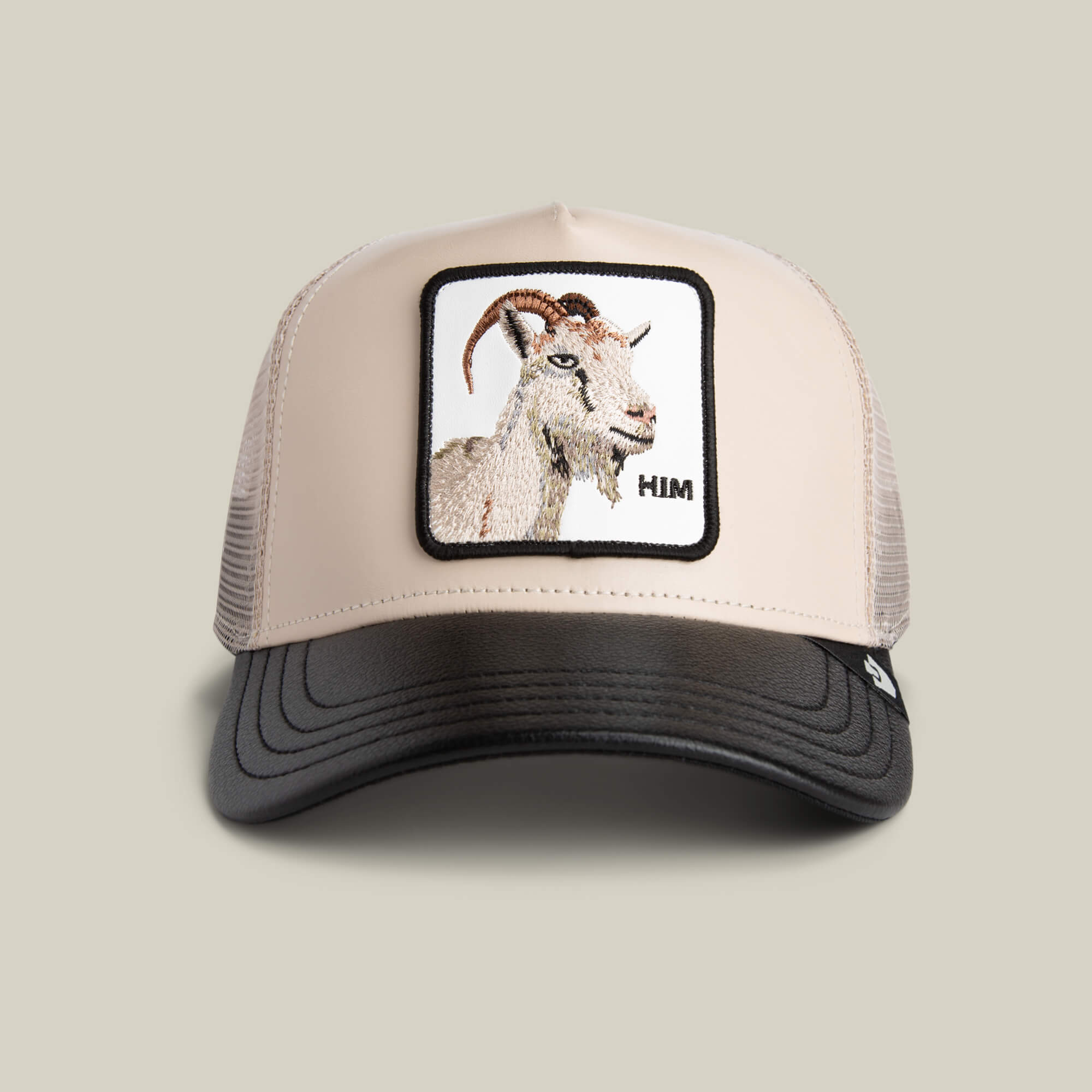 The Goorin Courtside Him trucker hat in TOAST/VOID features a mesh back, faux leather GOAT patch of a goat’s head, and "HIM" embroidered on the front.