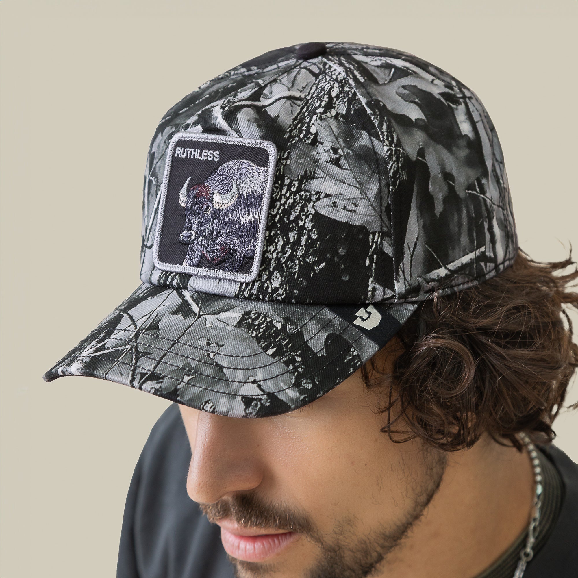 Man wearing a Goorin Bros. Ruthless Camo cap, featuring a black and grey camo pattern and a front patch with a bison and “RUTHLESS” text.