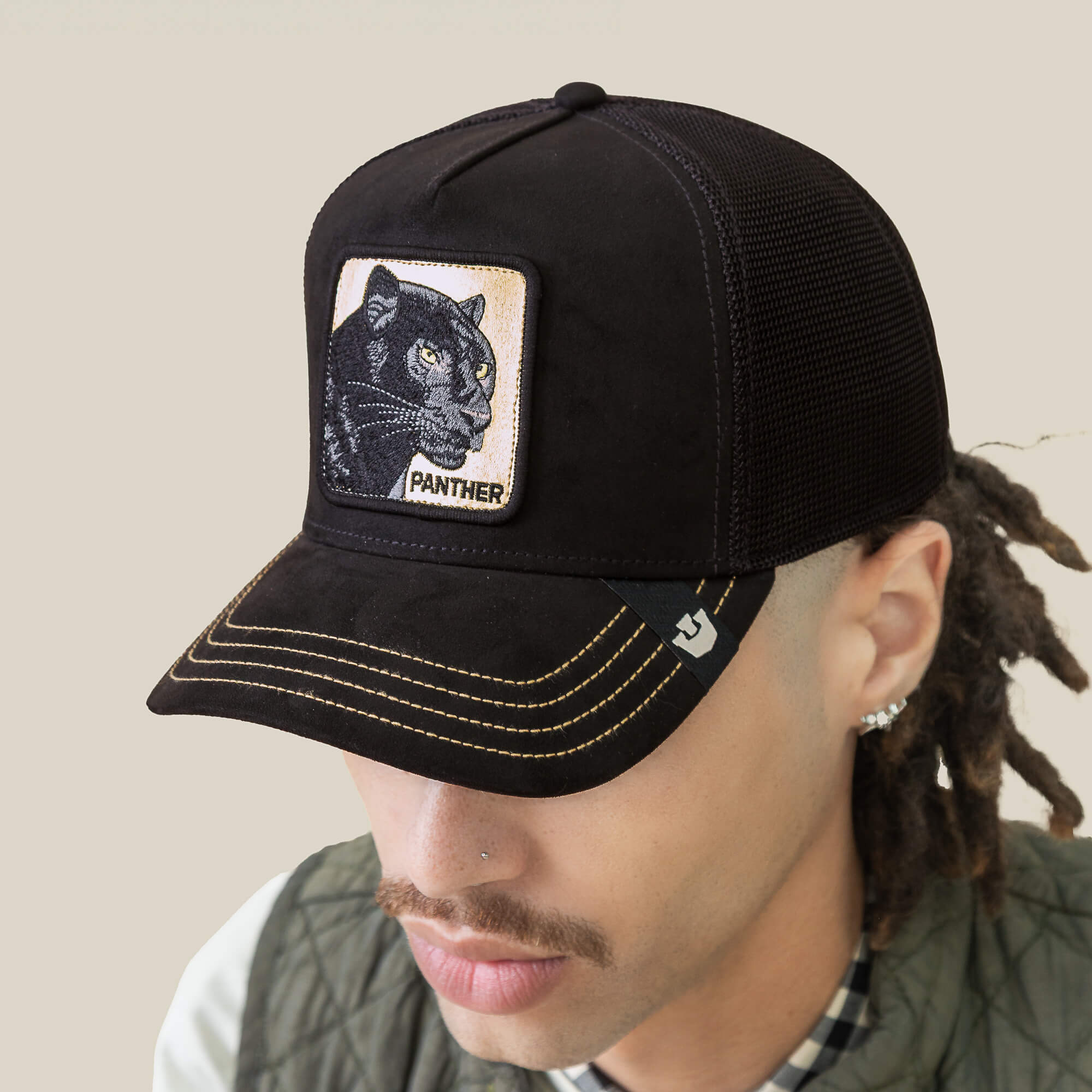 A person wearing the Goorin Bros. Golden Panther black stealth hat with a yellow-stitched microsuede crown and Golden Panther patch, looking downward.
