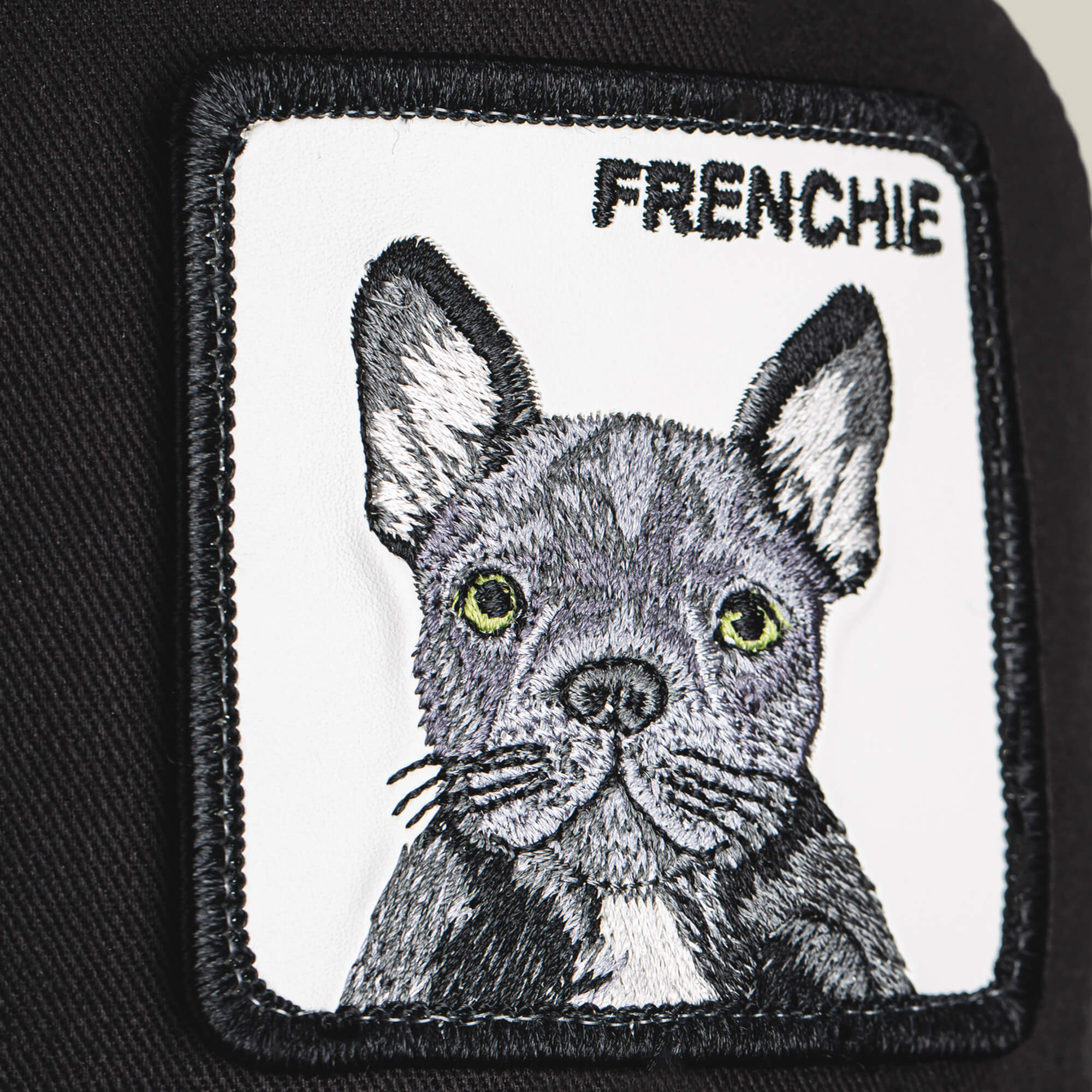 Close-up of The Frenchie Dog patch from Goorin Bros., featuring an embroidered French bulldog and the word FRENCHIE, sewn onto black fabric—ideal for any dog lover’s trucker hat or cap collection.