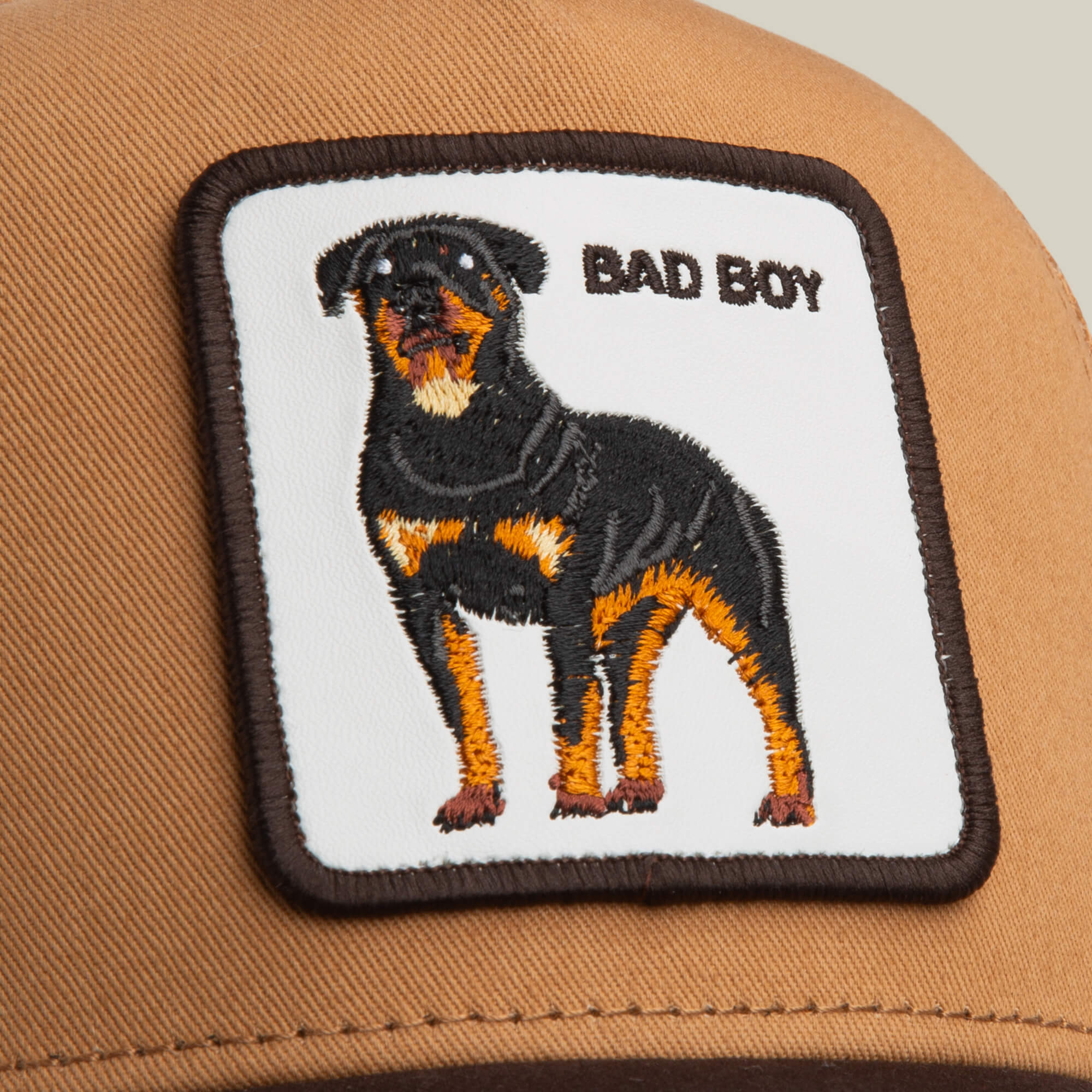 The Bad Boy by Goorin Bros. is a stylish brown cap with a square patch featuring an embroidered Rottweiler and BAD BOY text on a white background.