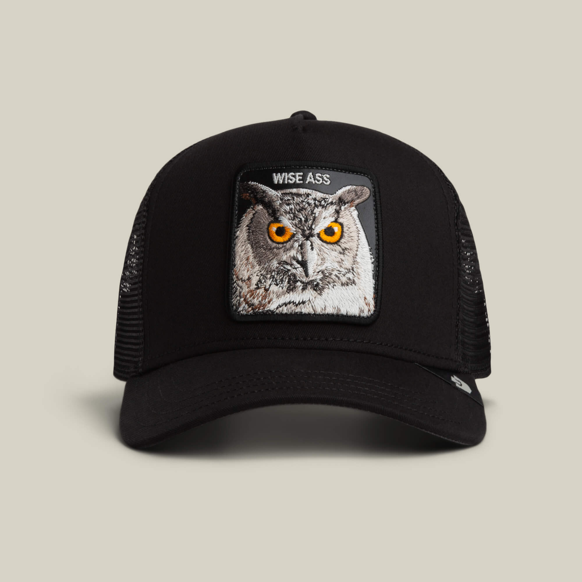 The Wise Ass Trucker by Goorin Bros. is a black mesh cap featuring an embroidered owl patch with orange eyes and the words "WISE ASS" above it.