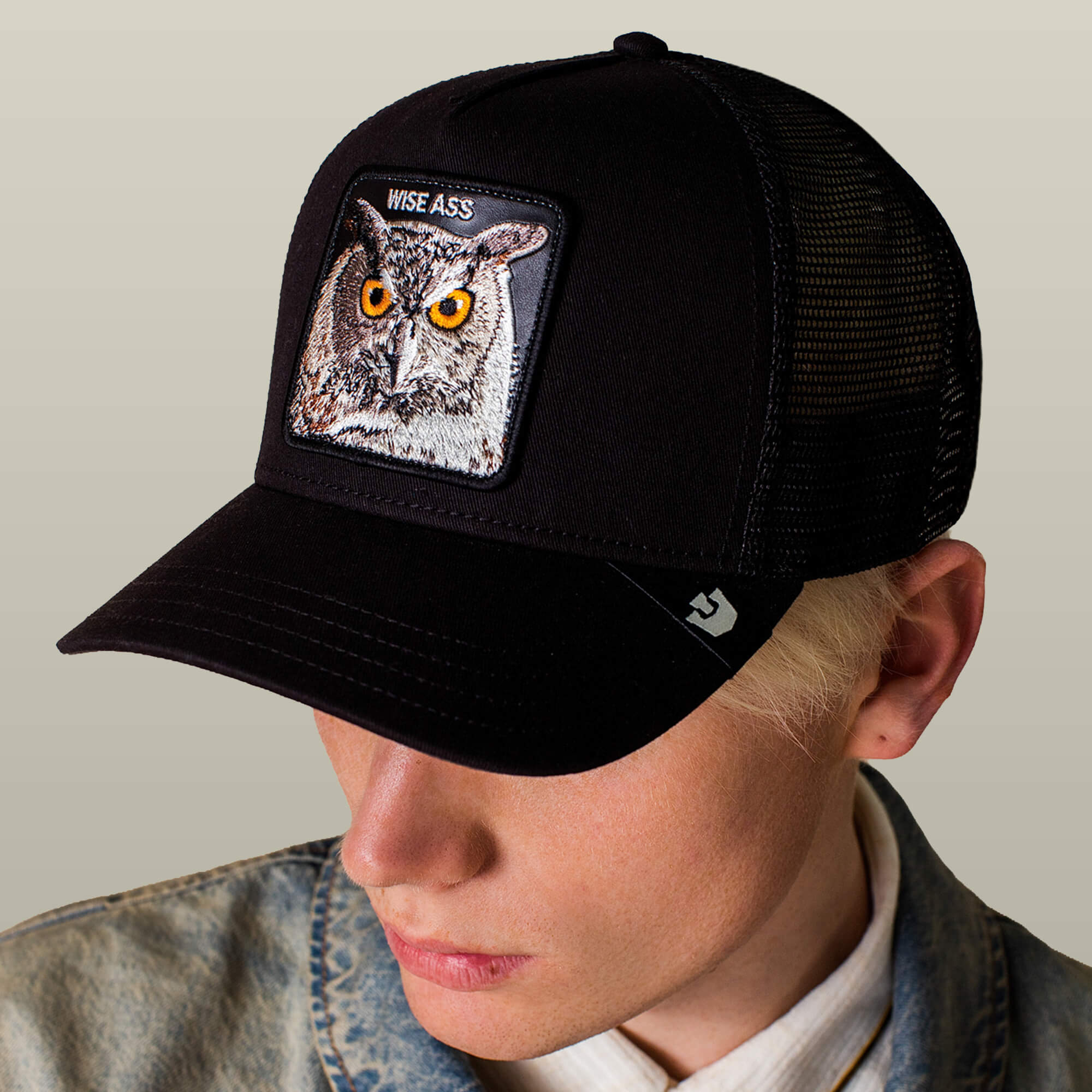 Person wearing the Goorin Bros. Wise Ass Trucker, a black mesh cap with an owl patch and "WISE ASS" text, looking downward.