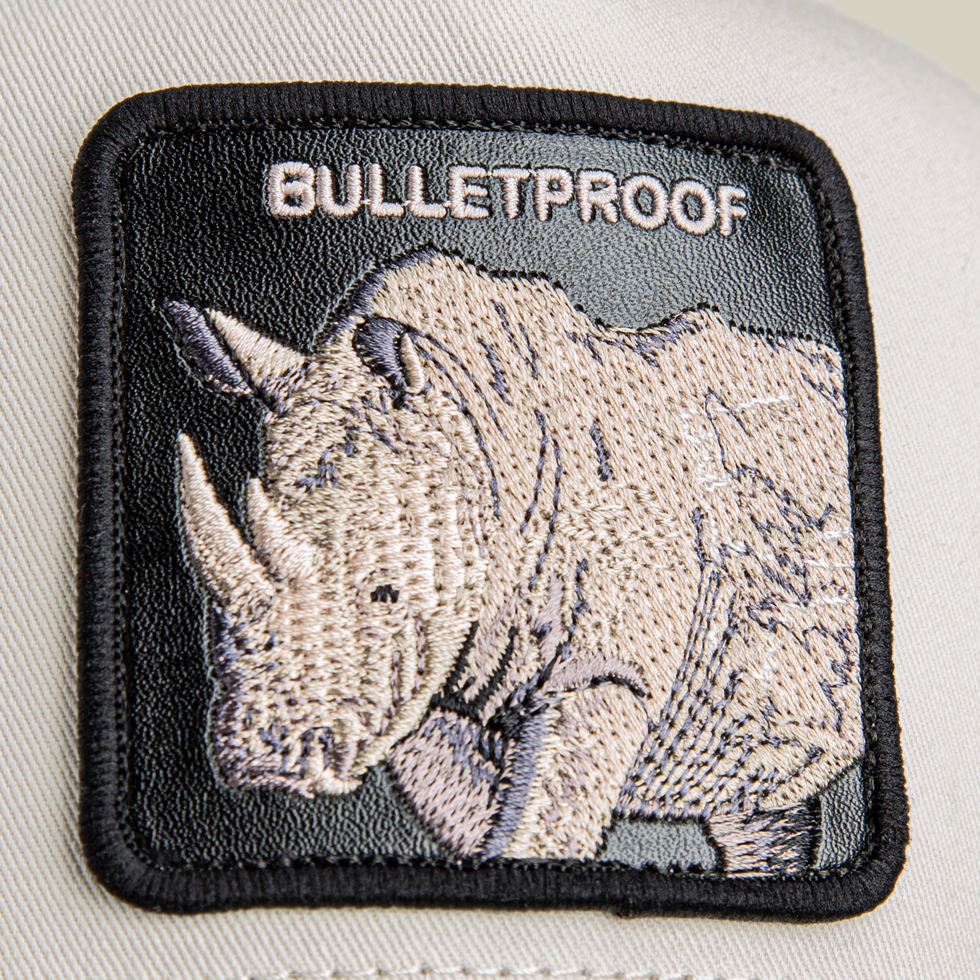 A close-up shows a patch on fabric featuring an embroidered rhinoceros with armor and "BULLETPROOF" above it, from the Bulletproof Trucker cap by Goorin Bros.