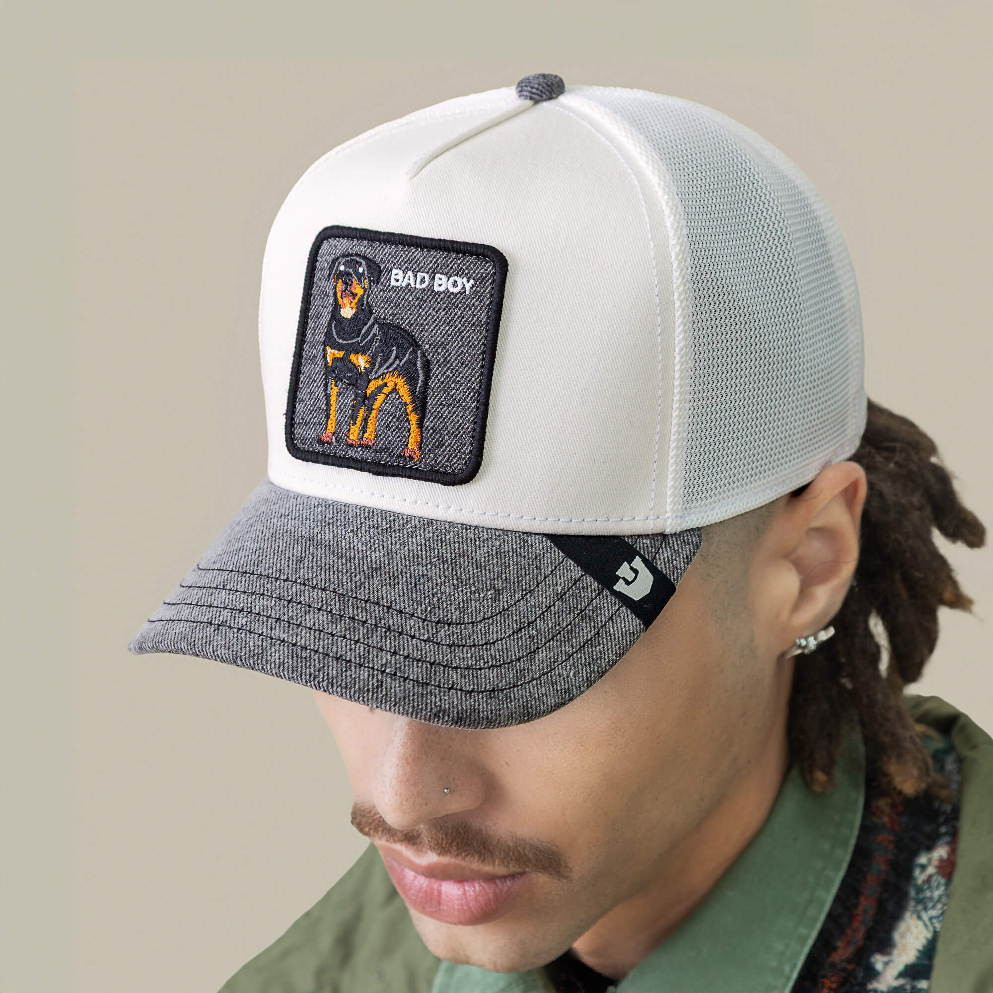 Man wearing the Goorin Bros. Denim Bad Boy cap—a light-colored mesh hat with a gray brim and a patch featuring an embroidered Rottweiler and "BAD BOY.