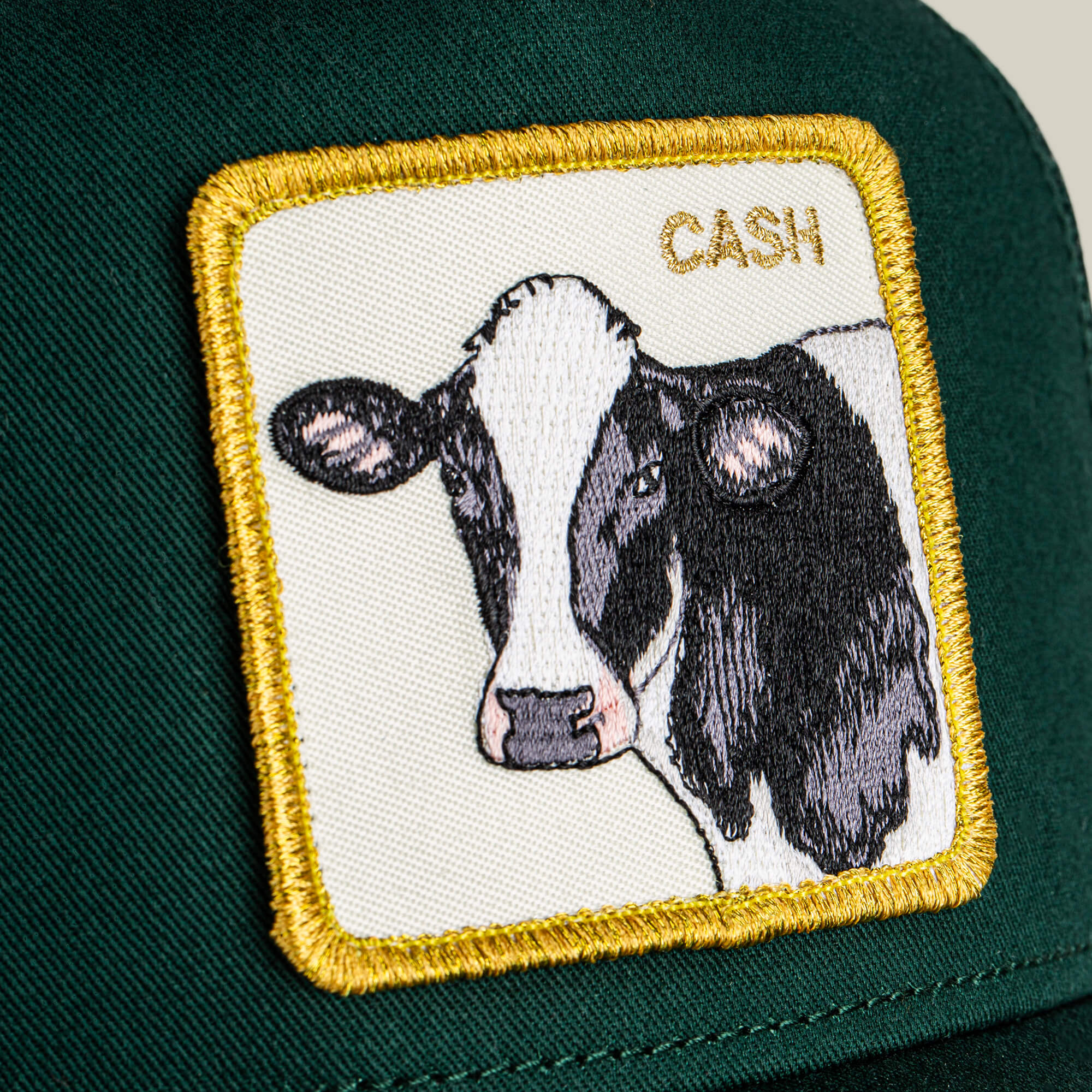 The Goorin Bros. Cash Cow Trucker is a green hat with a patch depicting an embroidered black and white cow and “CASH COW” in gold lettering at the top right.