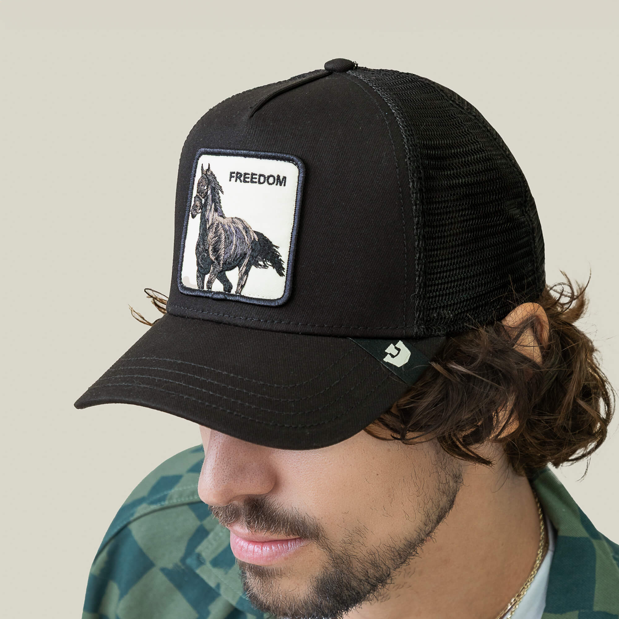 A man wears the Goorin Bros. Freedom Horse black mesh baseball cap, featuring a horse trucker patch with a running horse and the word "FREEDOM," embodying the wild spirit of open roads.