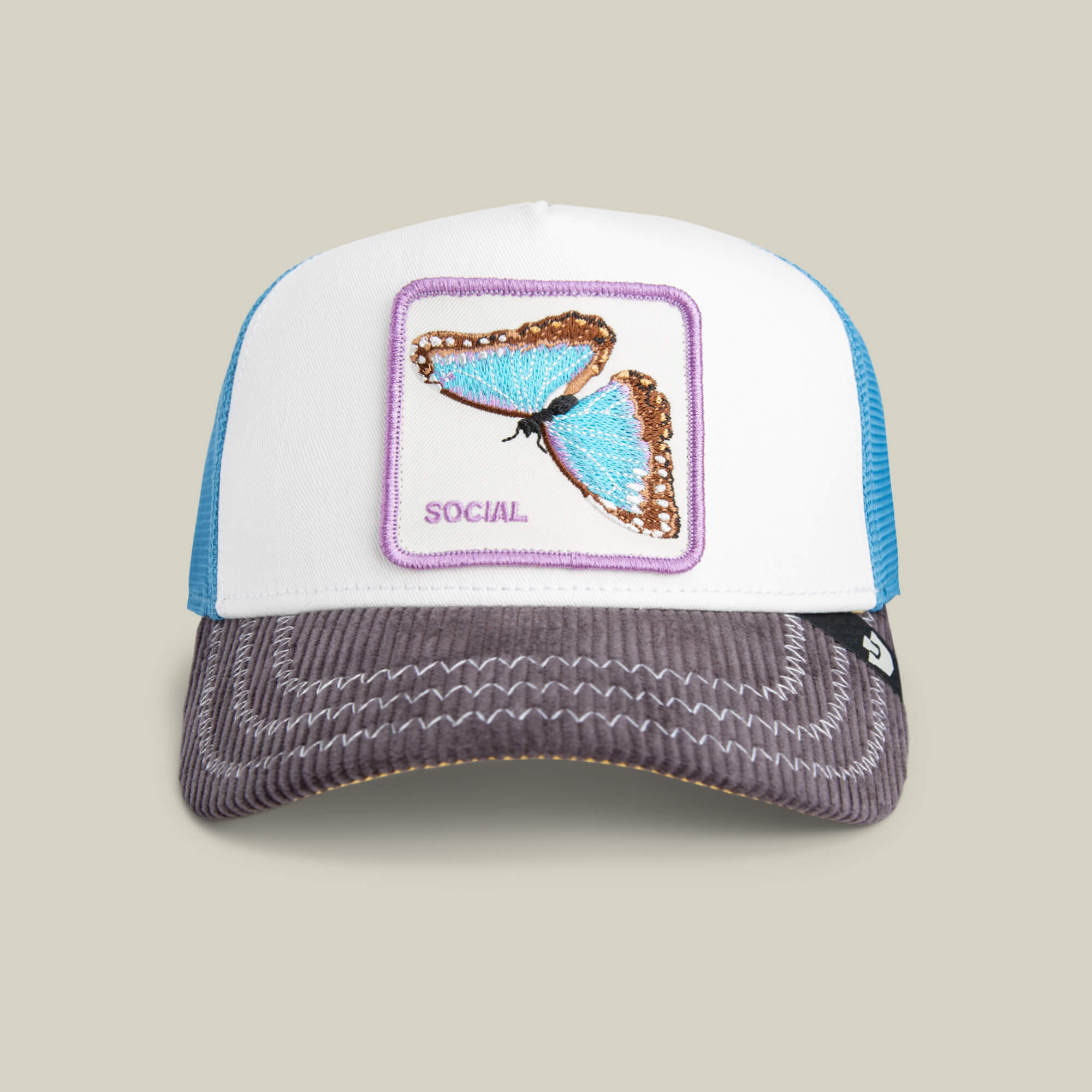 The Goorin Bros. Social Remix trucker hat features a blue butterfly patch labeled SOCIAL, a blue mesh back, and a gray corduroy brim with white stitching—ideal for standout style.
