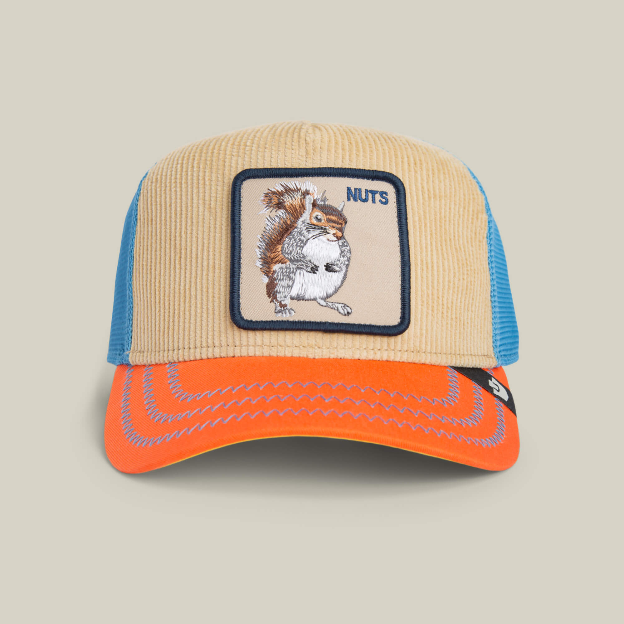 Add forest flair to your look with the Goorin Bros. Nuts Remix trucker hat—tan corduroy, electric blue mesh, orange brim, and a patch of a squirrel holding a nut with “NUTS” embroidered on the front.