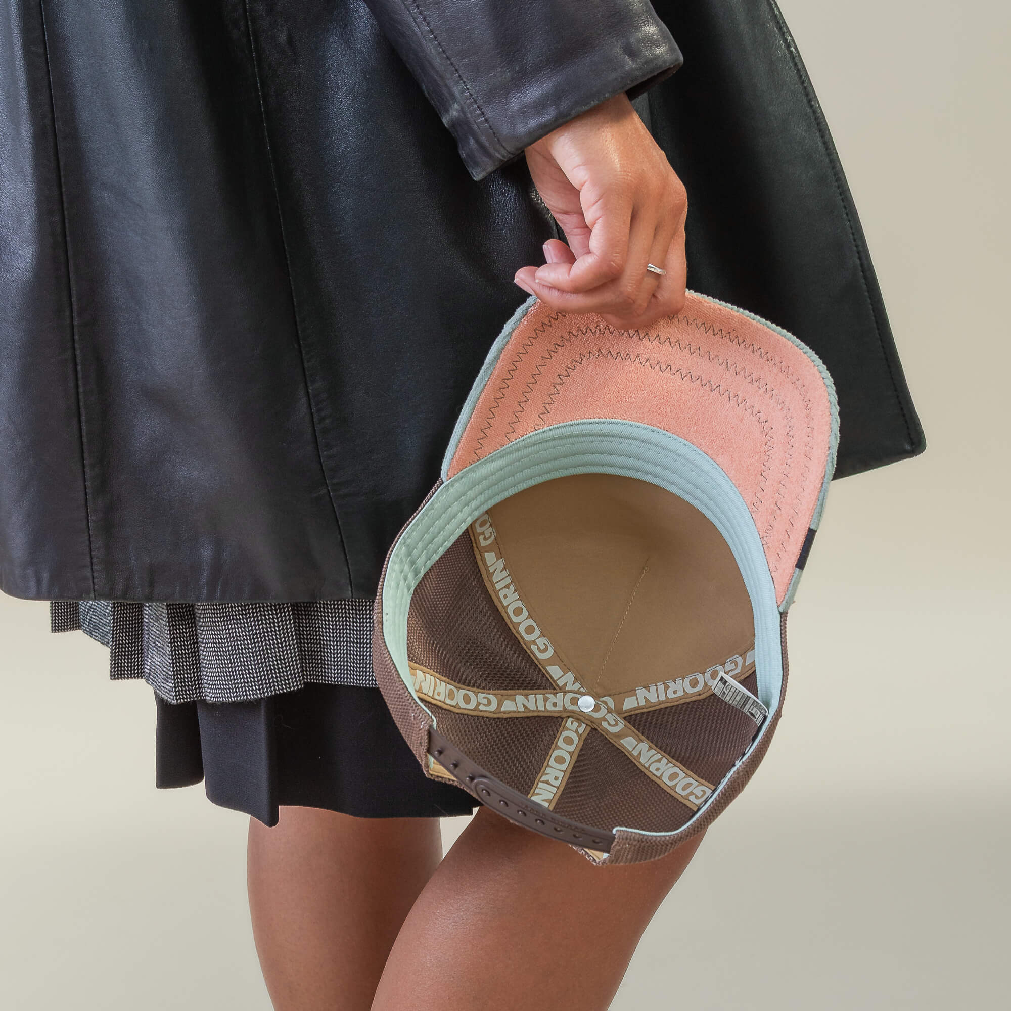 A person in a black coat holds an upside-down Goorin Bros. Faded Remix cap with a pink brim and "GOOD MORNING" inner straps, giving off the playful vibe of a cream corduroy hat.