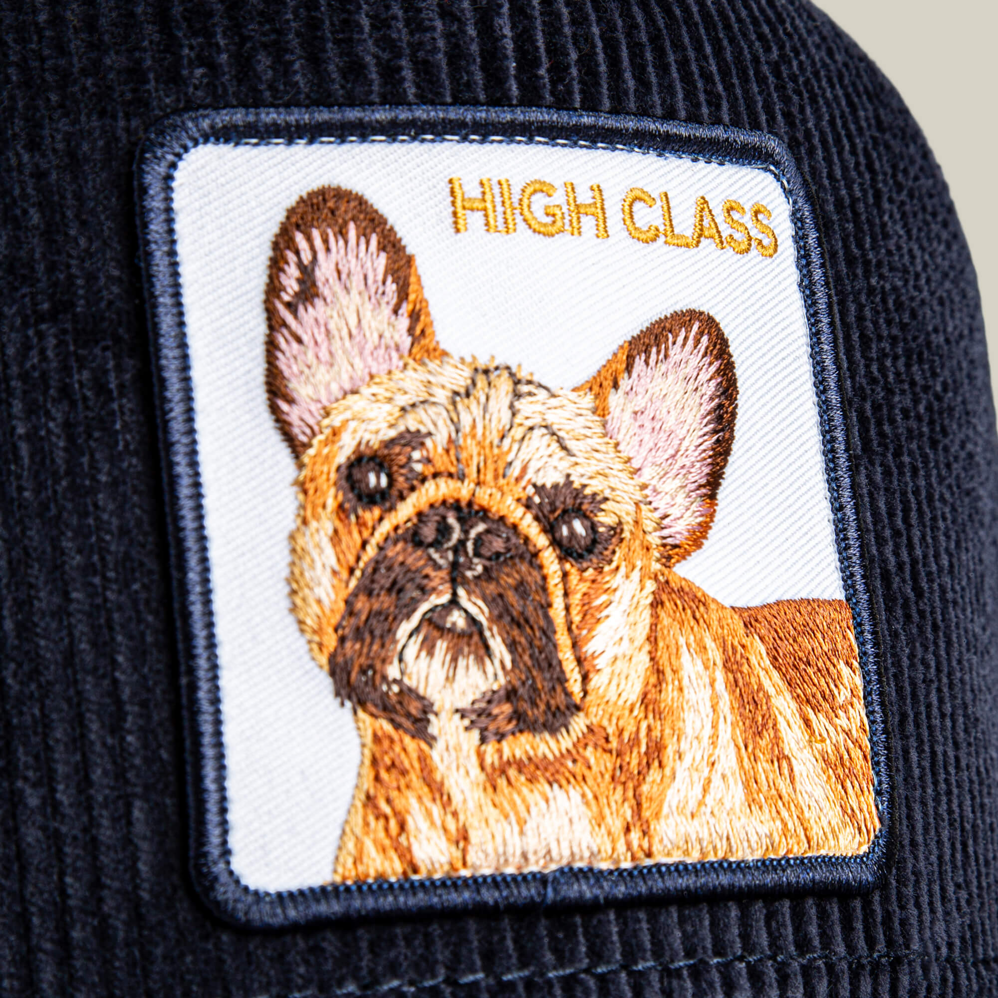 The High Class Remix by Goorin Bros. is a navy blue corduroy hat with rich textures, showcasing an embroidered French bulldog patch and "HIGH CLASS REMIX" in gold lettering.