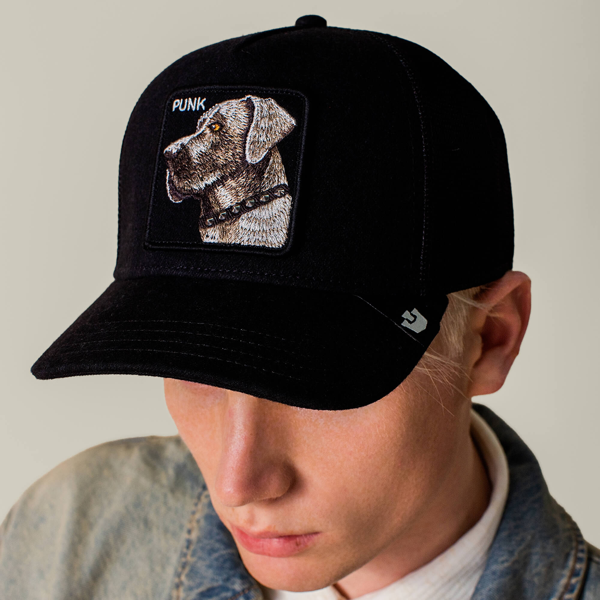 A person wearing Goorin Bros.’ Punk Dawg black cap, featuring a dog head patch labeled "PUNK," pairs it with a light denim jacket and white shirt—embodying the bold attitude of the Punk Dawg collection.