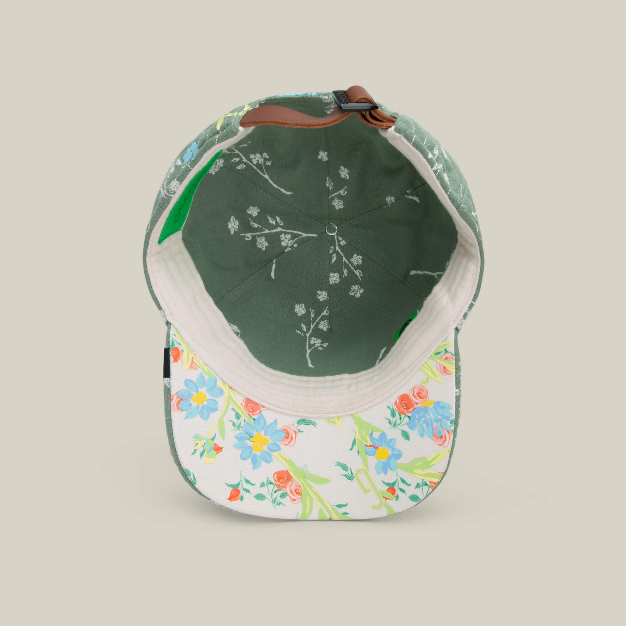 The Goorin Bros. Vol. 1 - Quiltbag: Laugh is a floral trucker hat seen from above, with a green inner lining featuring white branches and a brim decorated with colorful patchwork-like flower designs.