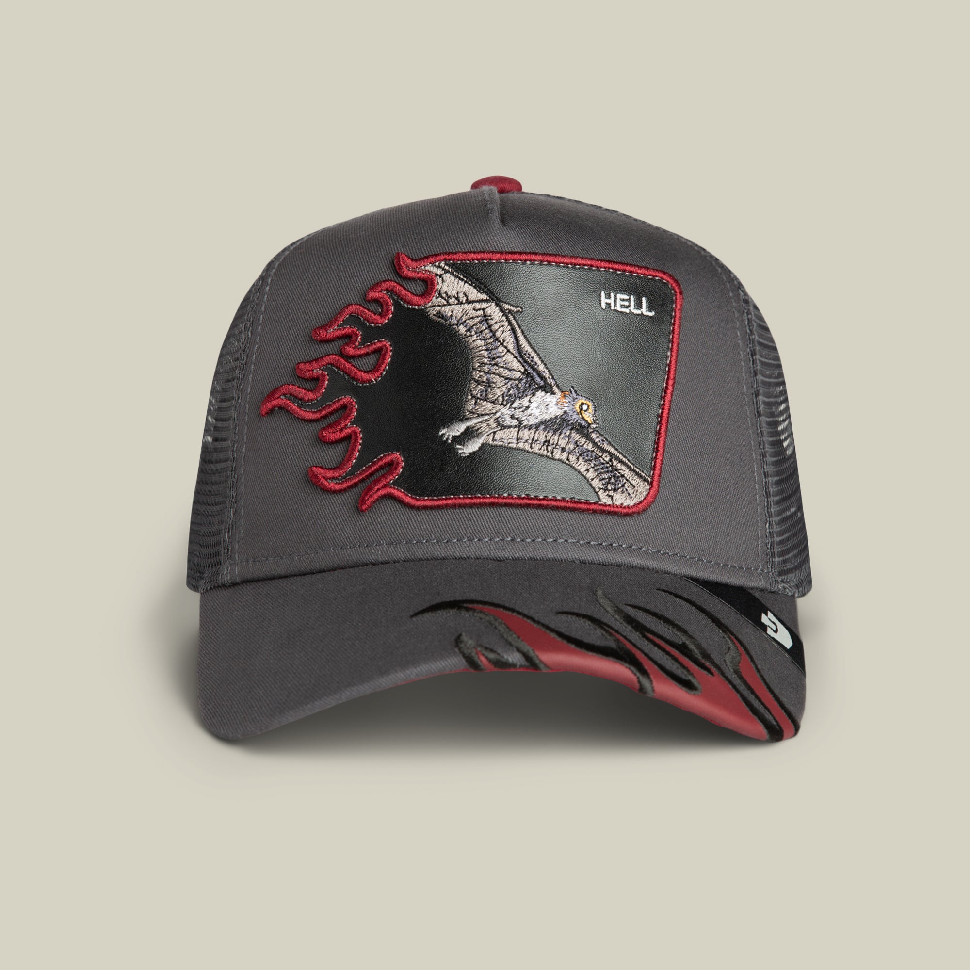 The Goorin Bros. Hell Flames trucker hat in OIL GRAY features a pterodactyl patch with red flames and the word "HELL," plus bold flame designs on the brim—making it a standout statement piece.