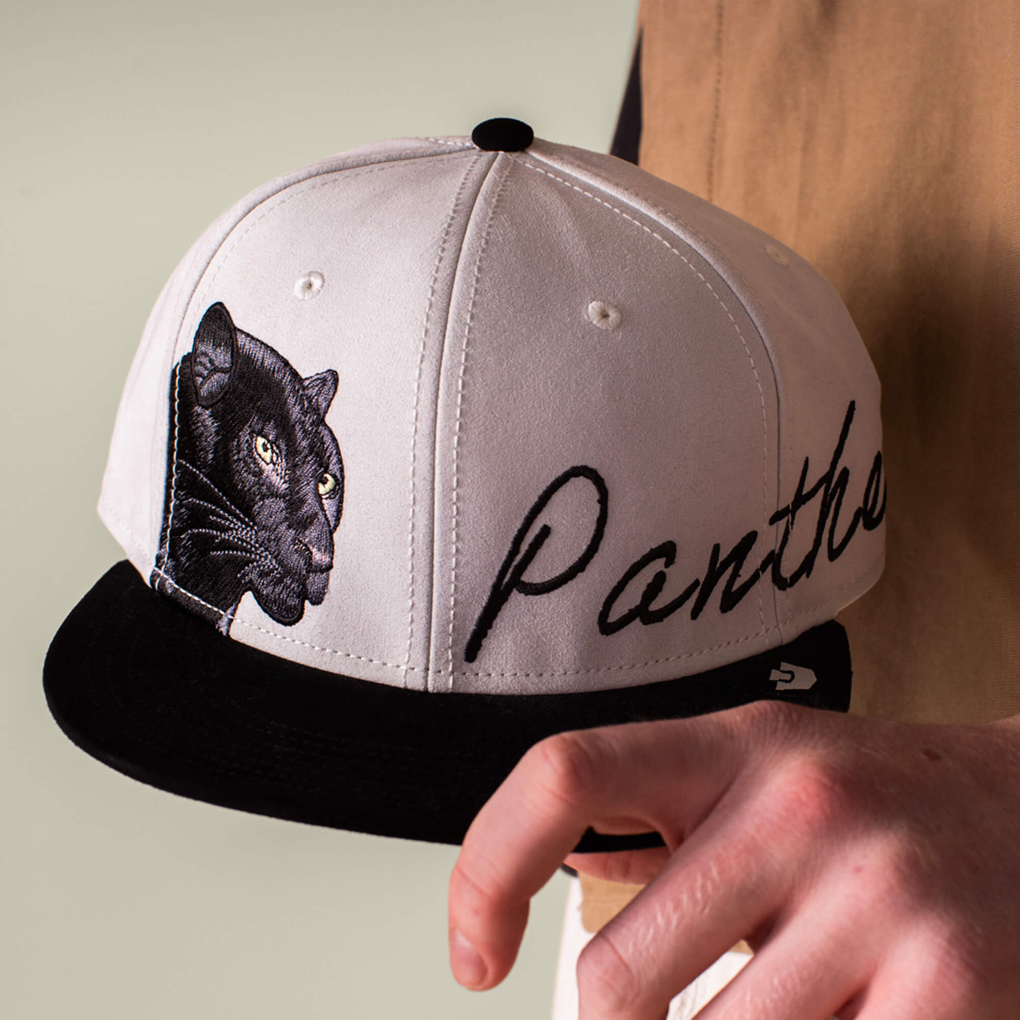 A person holds the Goorin Bros. 6-Panel Panther Script cap, a black and white hat with an embroidered panther patch featuring a black panther face and "Panther" in cursive.