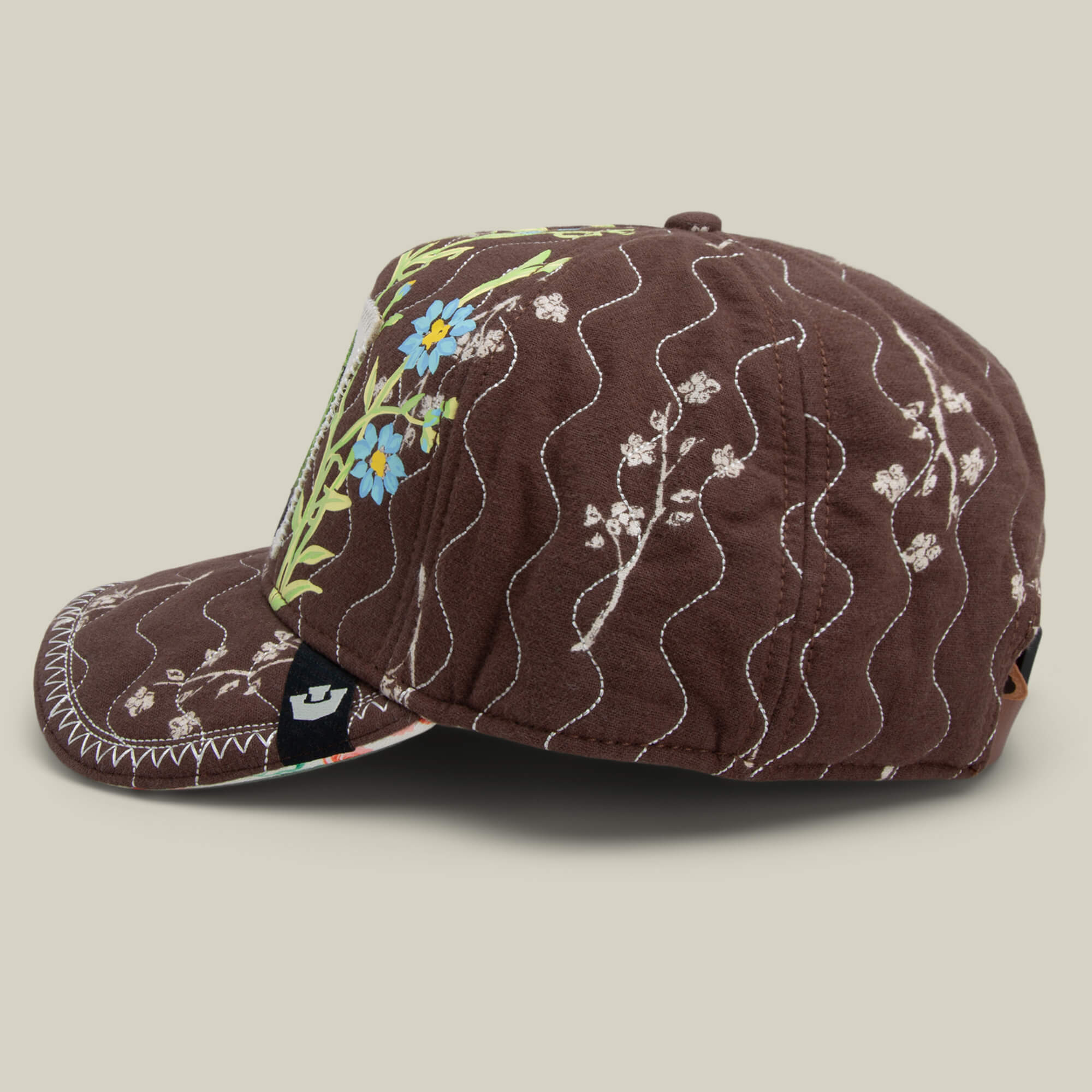 The Vol. 1 - Quiltbag: Love cap by Goorin Bros. features hand-stitched white wavy accents and blue and yellow floral embroidery, displayed from the side against a neutral background.