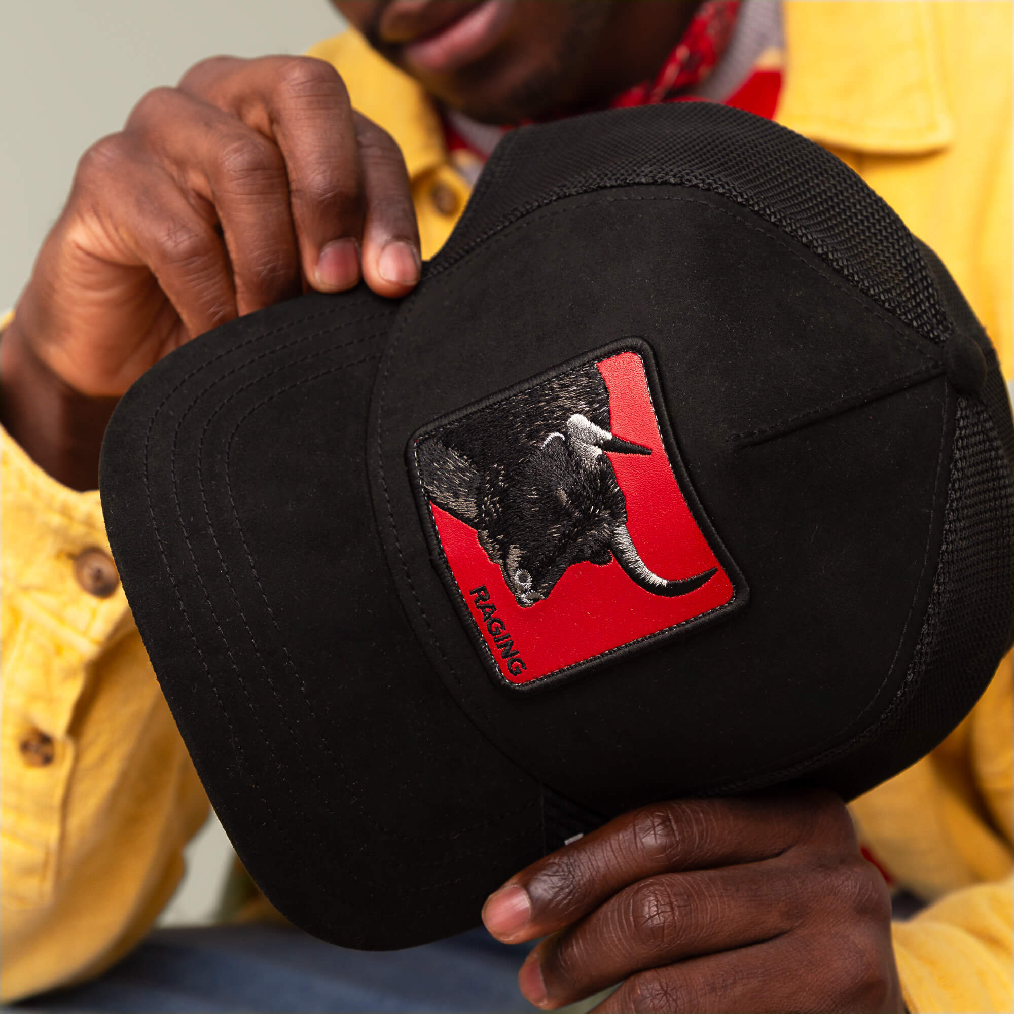A person in a yellow jacket holds the Toro Rosso trucker hat by Goorin Bros., featuring a bold patch with a black bull on a red background, capturing the fierce spirit of the collection.