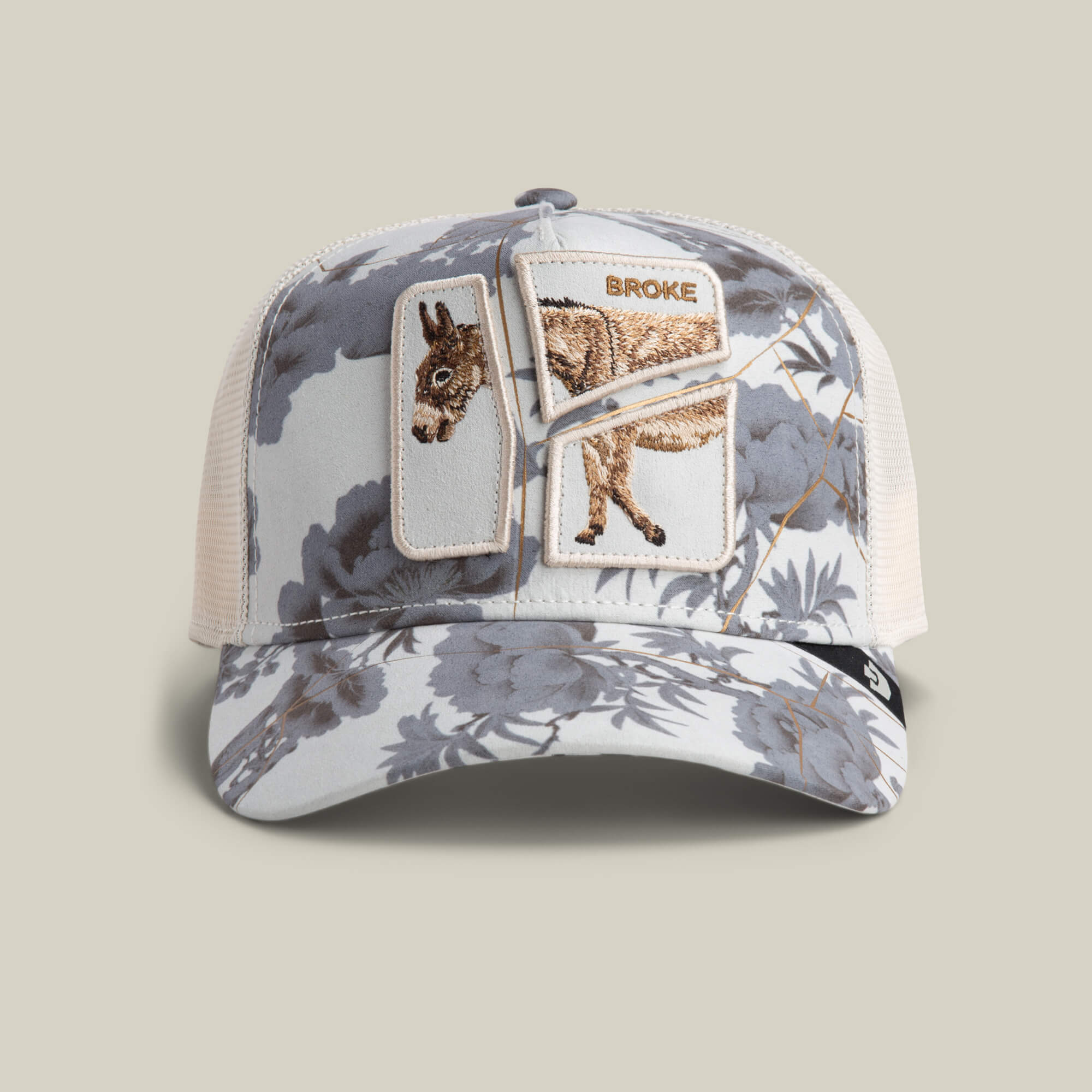The Goorin Bros. Break The Bank mesh baseball cap in CHALK features a floral pattern and an embroidered donkey patch labeled BROKE—an amusing novelty gift for anyone with a playful sense of humor.