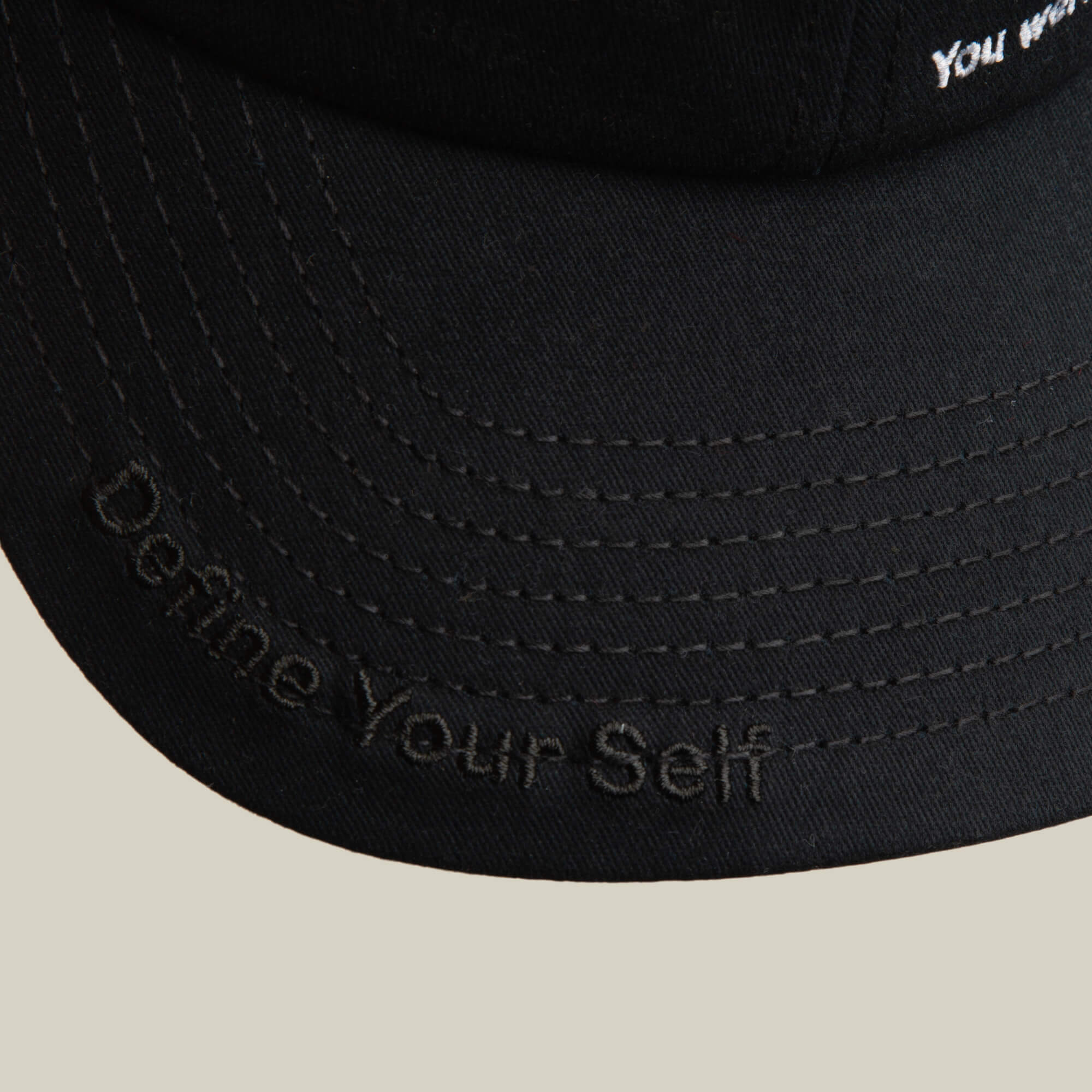 Close-up of the Goorin Bros. Define Yourself - Black Sheep hat featuring "Define Your Self" embroidered in black on the brim, highlighting its classic low profile cap design.