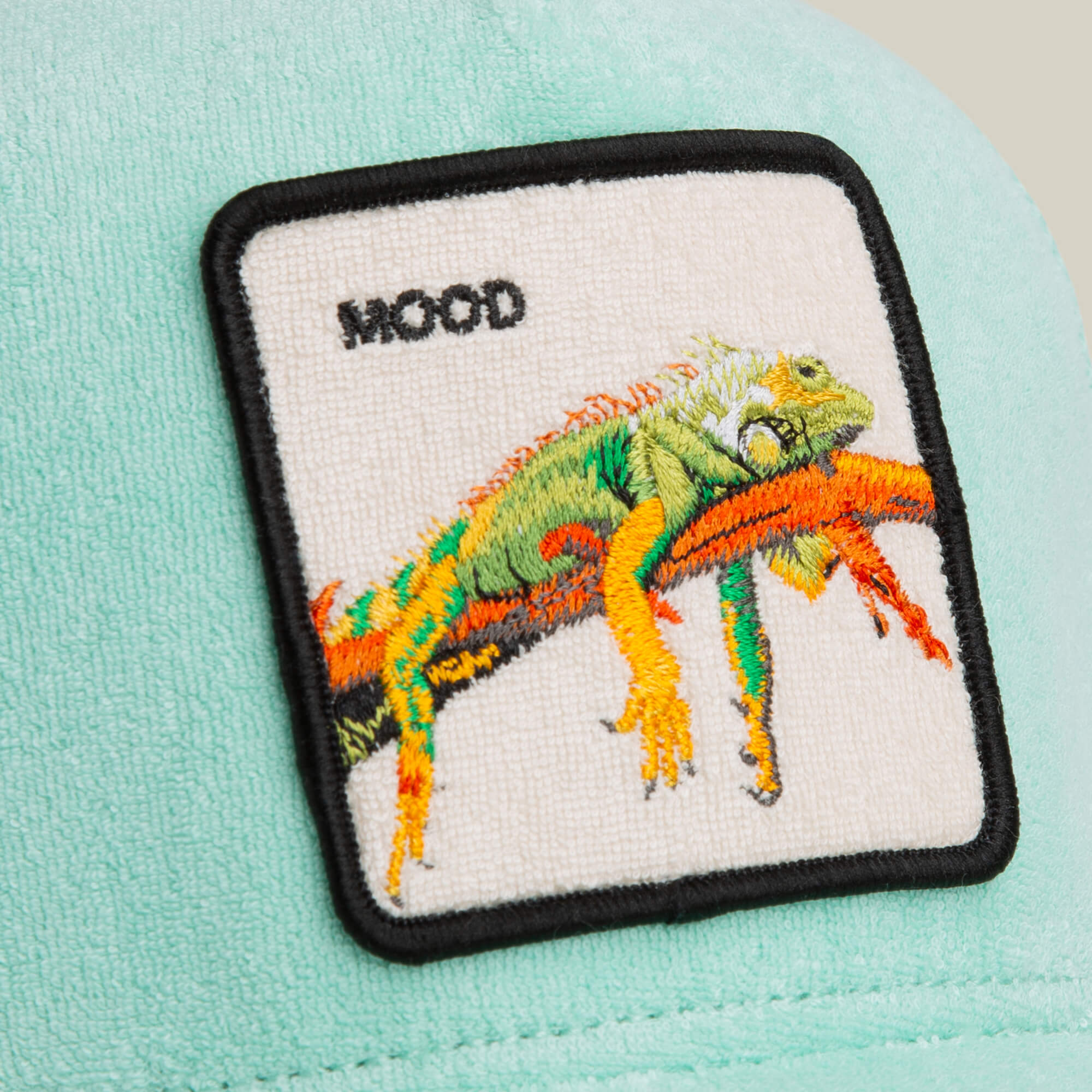 The Goorin Bros. Terry Cloth Iguana hat features a light green terry cloth trucker design and a patch with an embroidered iguana on a branch and the word "MOOD," adding playful style to this unique cap.