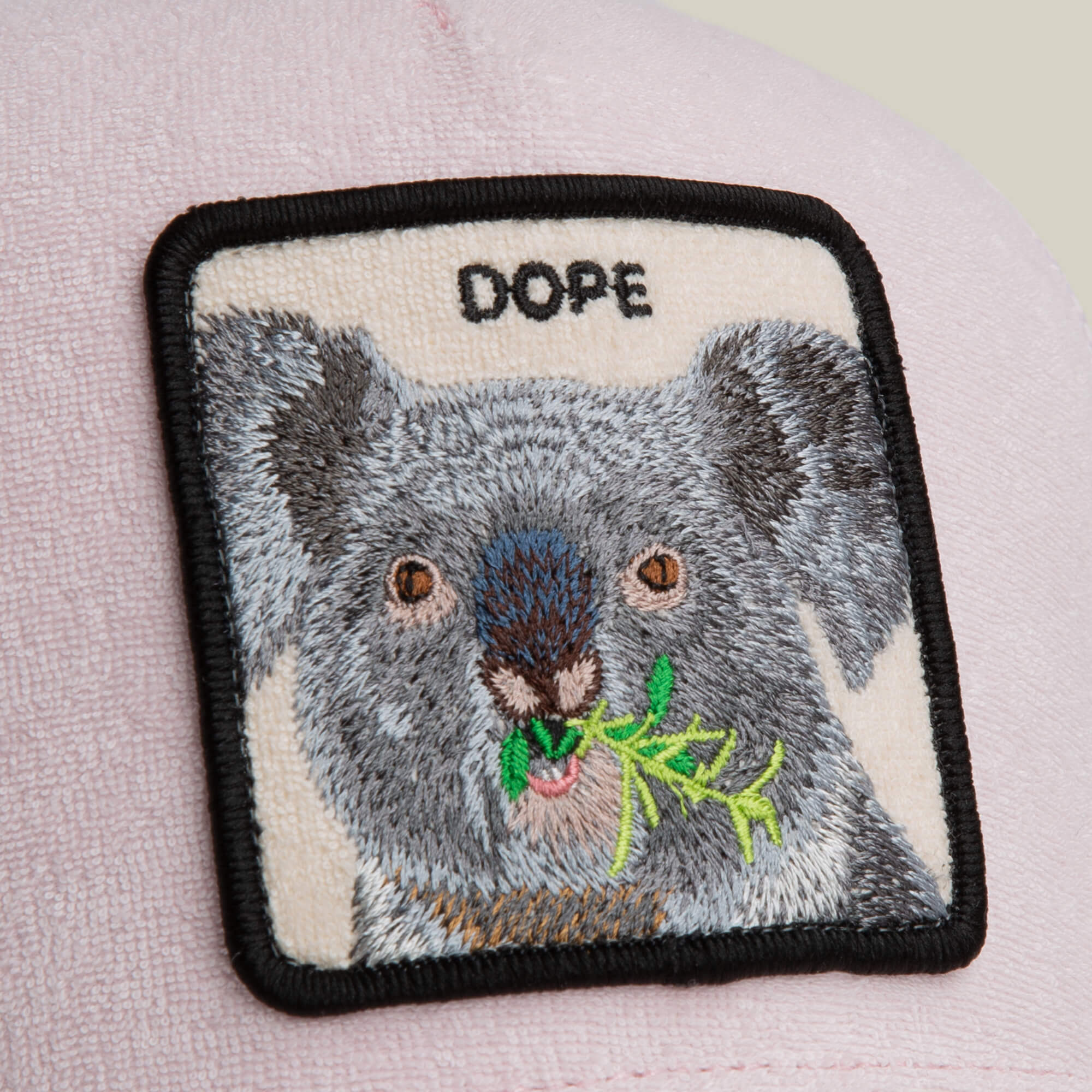 A cozy pale pink hat by Goorin Bros., the Terry Cloth Koala, features a soft square patch showing a koala eating leaves with "DOPE" above it.